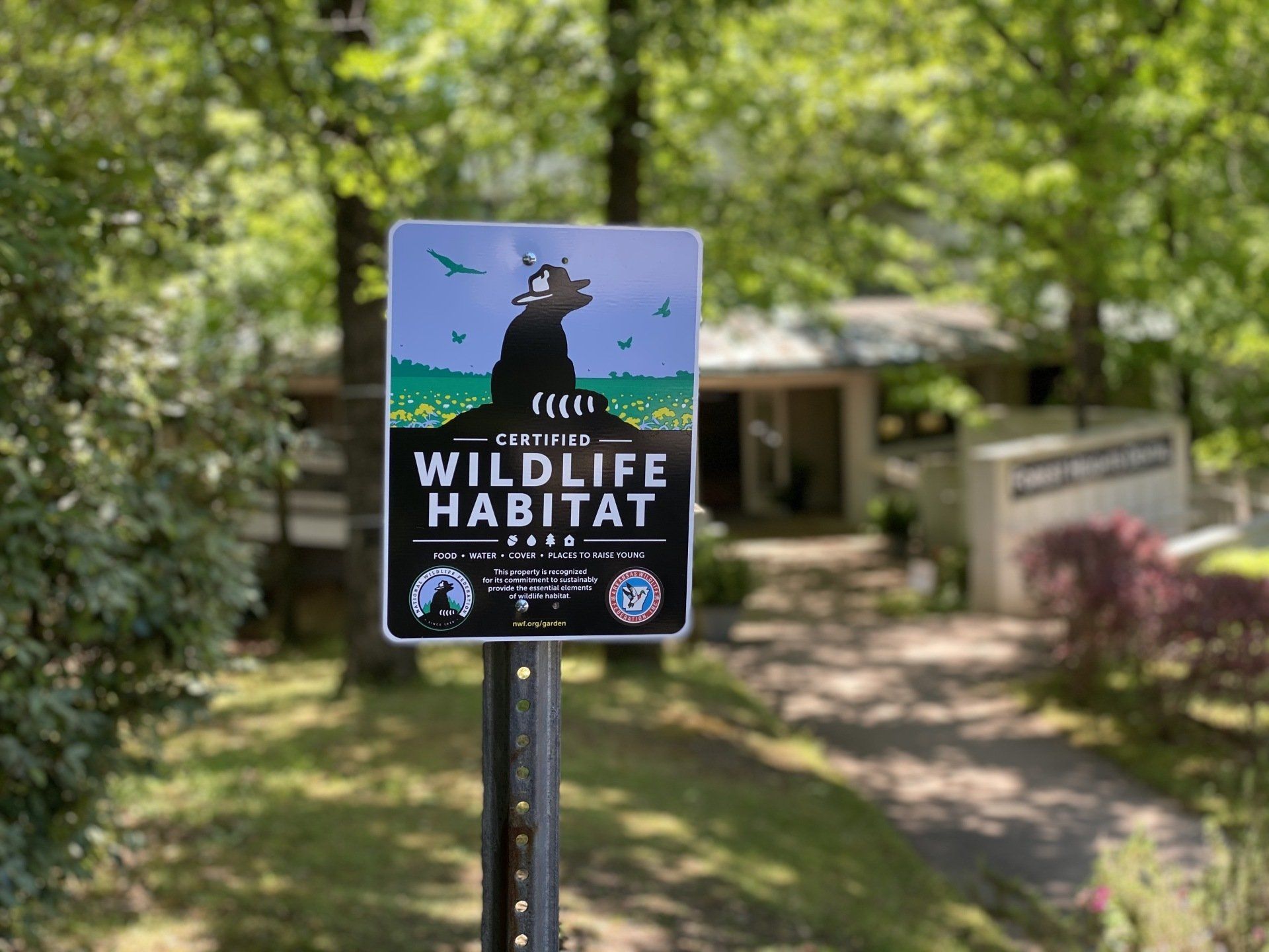 A wildlife habitat sign is on a pole in front of a house.