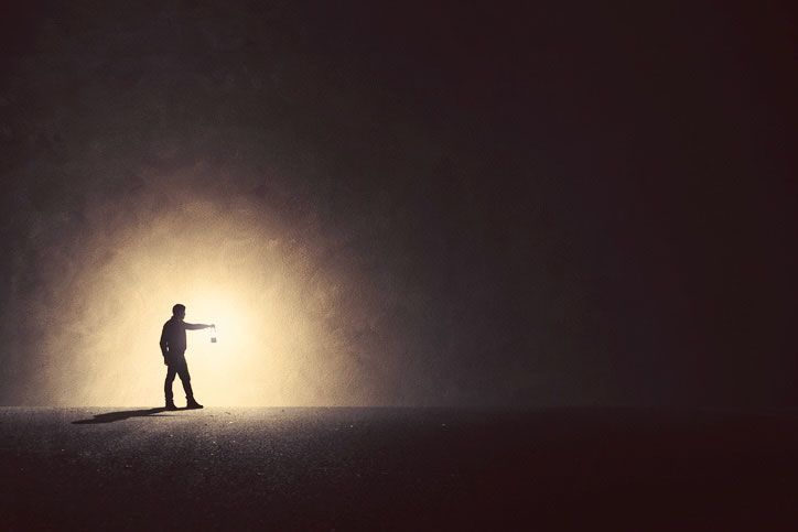 A silhouette of a man standing in front of a light in the dark.