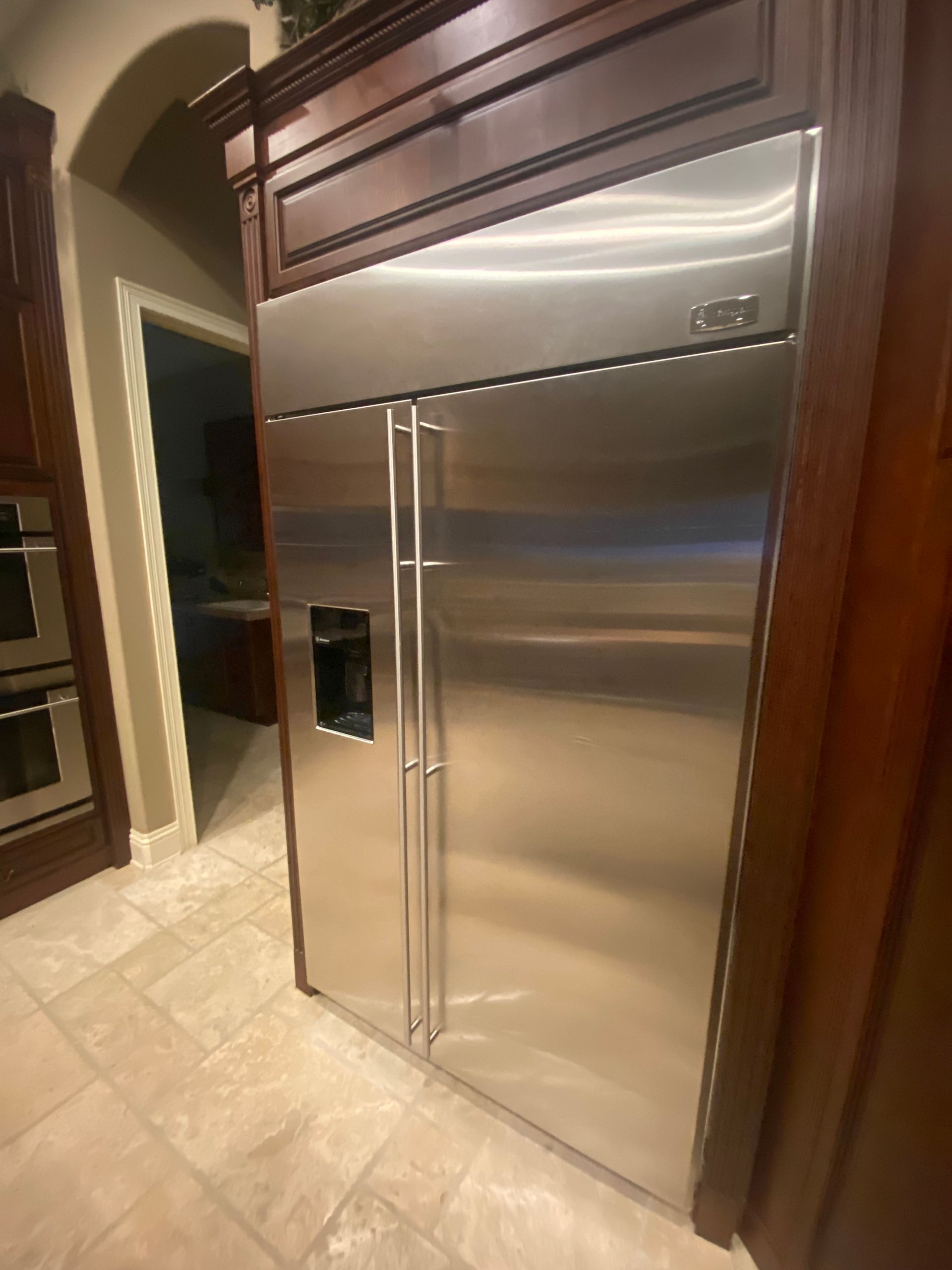 Stainless steel side-by-side refrigerator built into dark wood cabinets with a water dispenser on the door, in a kitchen.