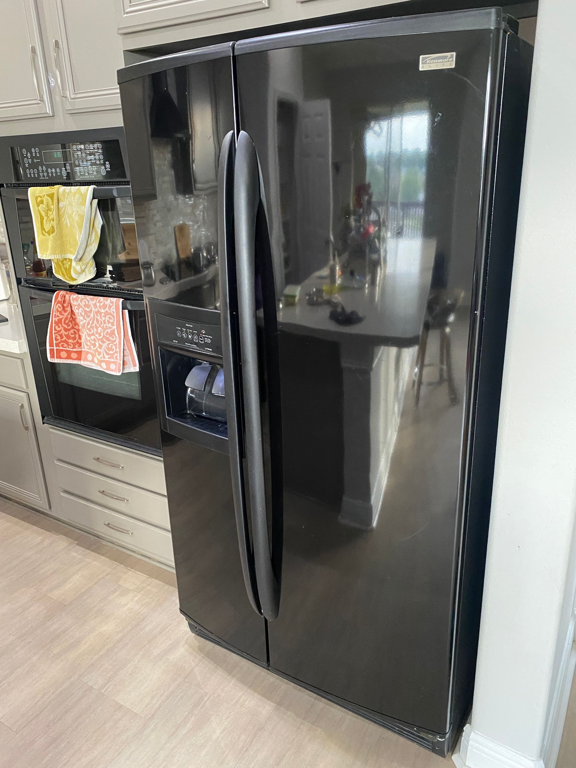 Black side-by-side refrigerator in a kitchen with a built-in oven and a countertop.