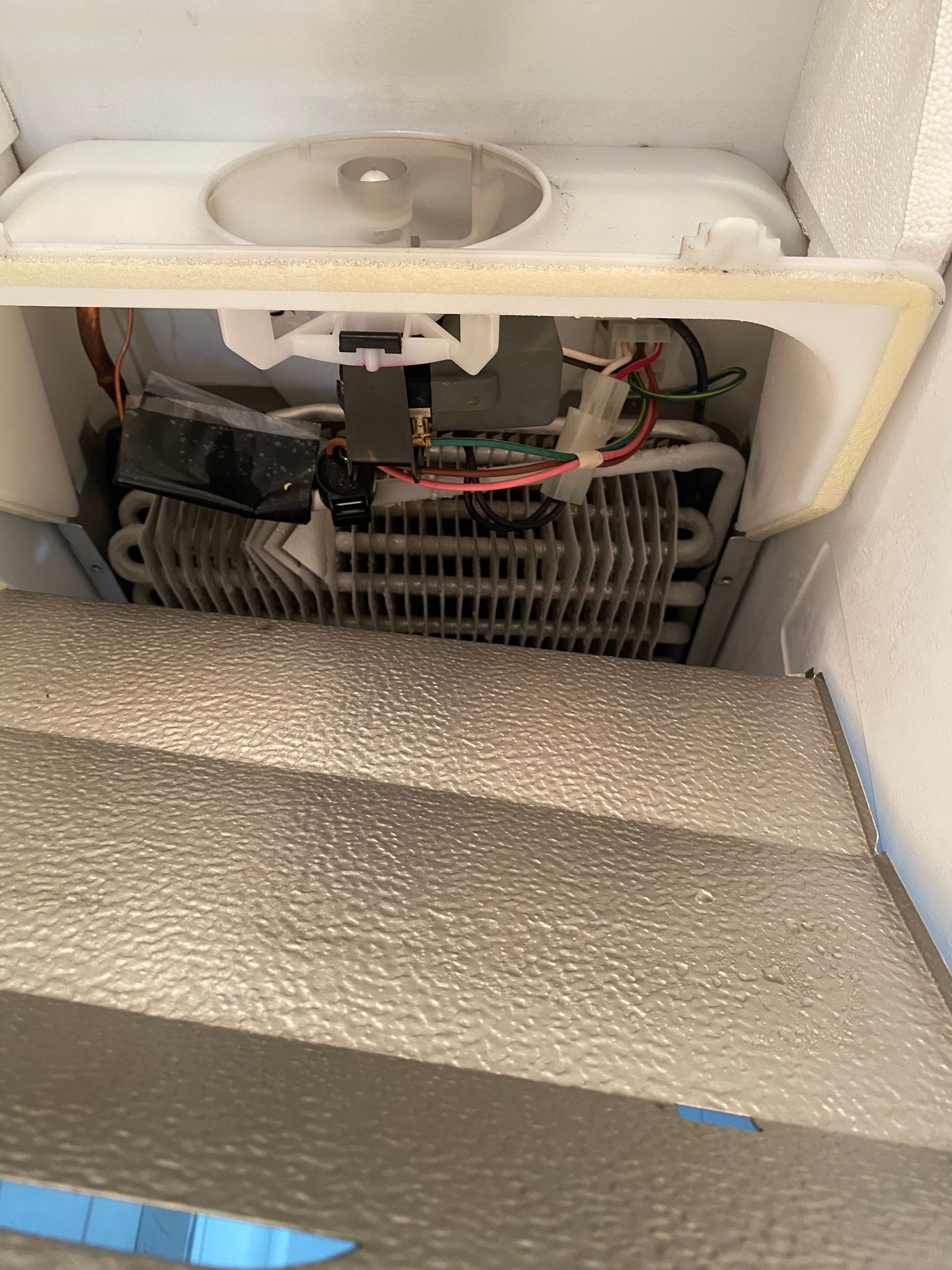 Inside a refrigerator, showing evaporator coils, fan, and wiring.