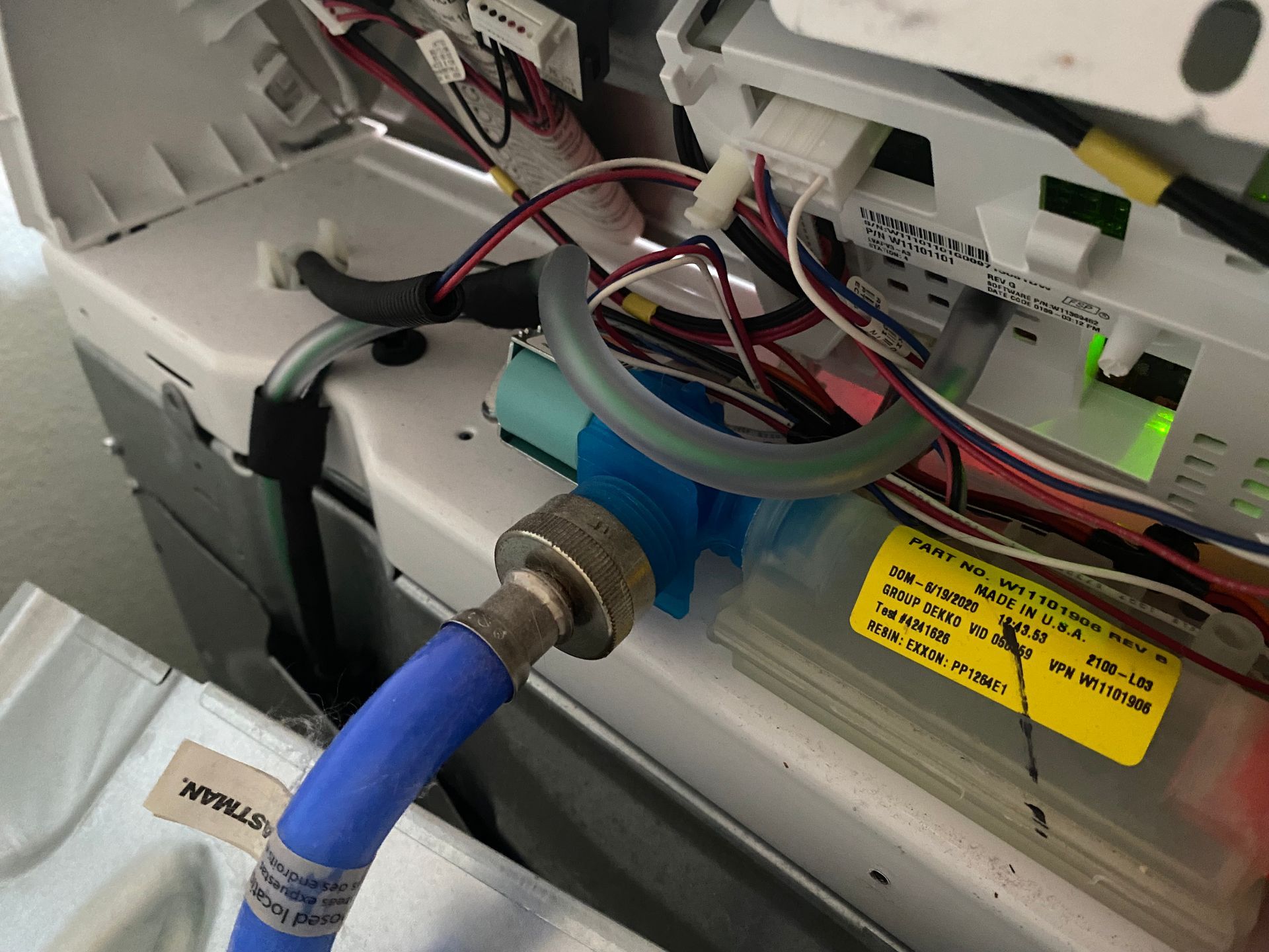 Close-up of a washing machine's water inlet valve and connected hoses, with wiring visible.