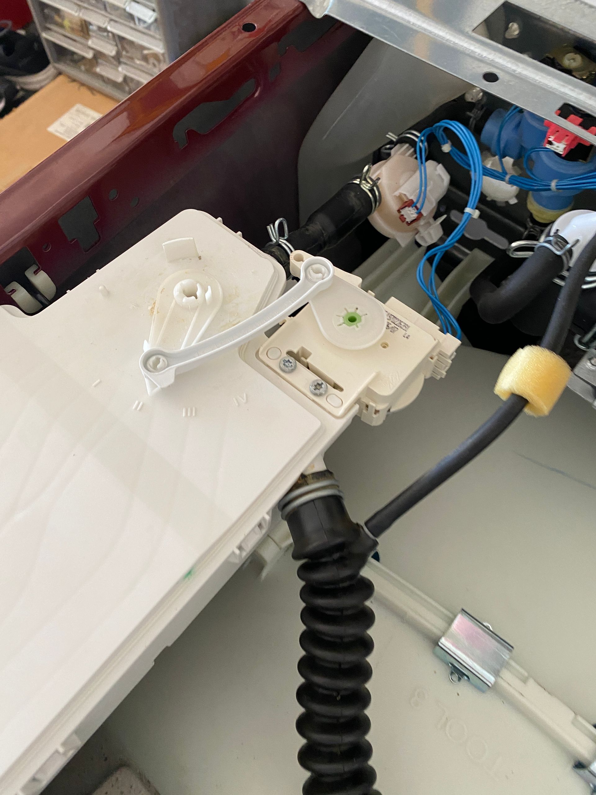 White appliance parts with a lever, connected hoses, and wires.