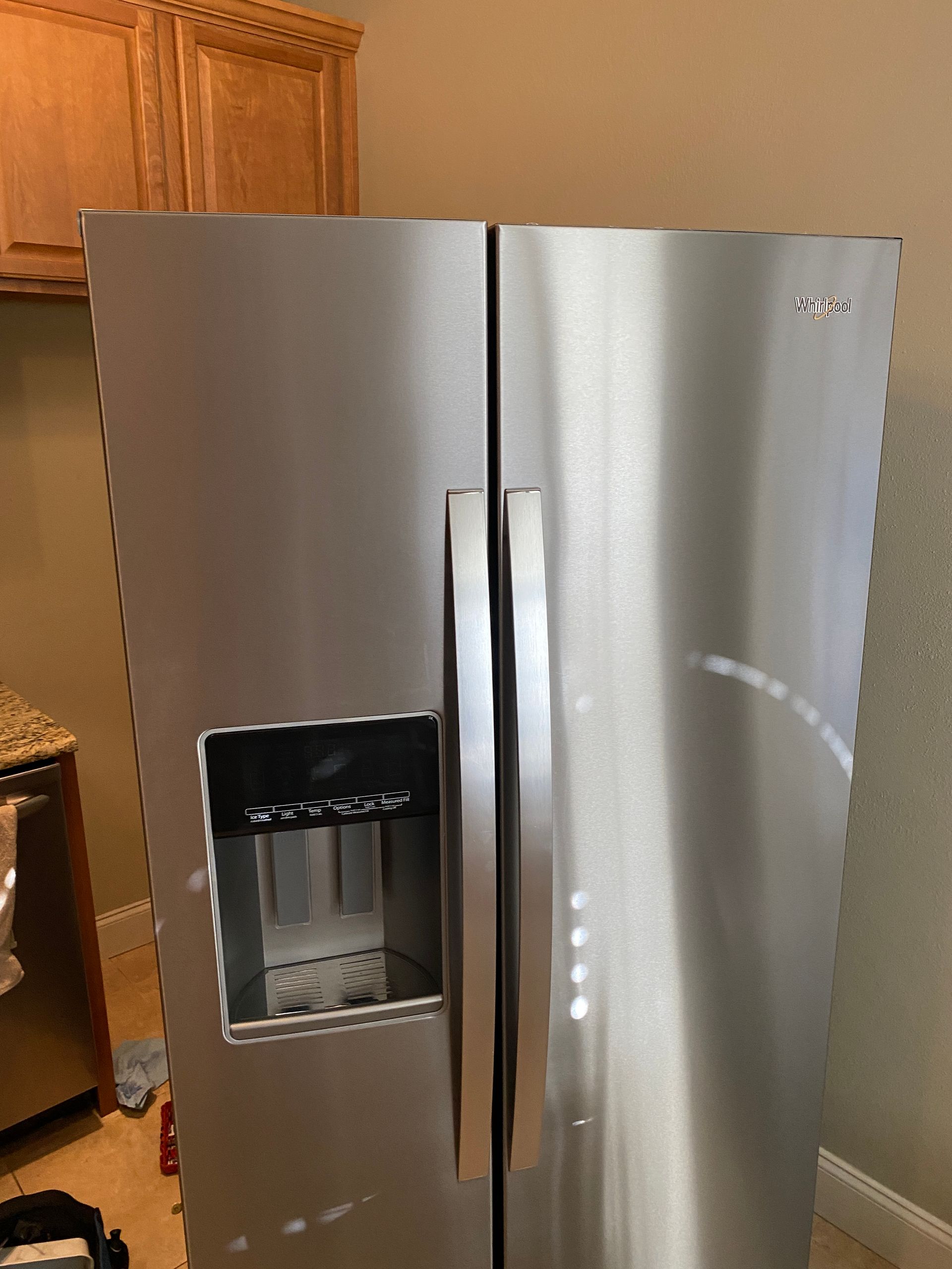 Stainless steel side-by-side refrigerator in a kitchen, with water dispenser and cabinet above.