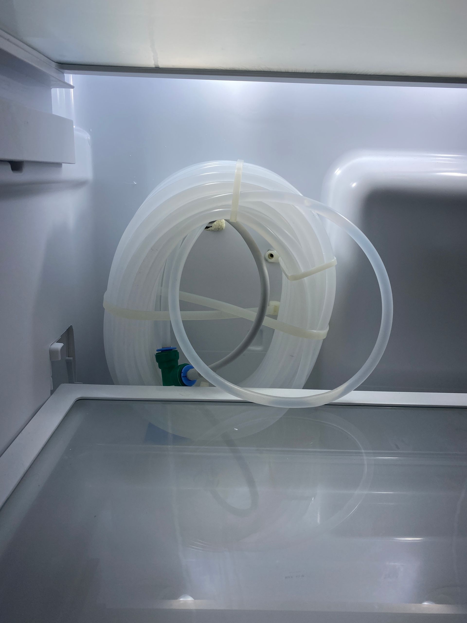 Coiled white tubing with a plastic fitting inside a refrigerator.