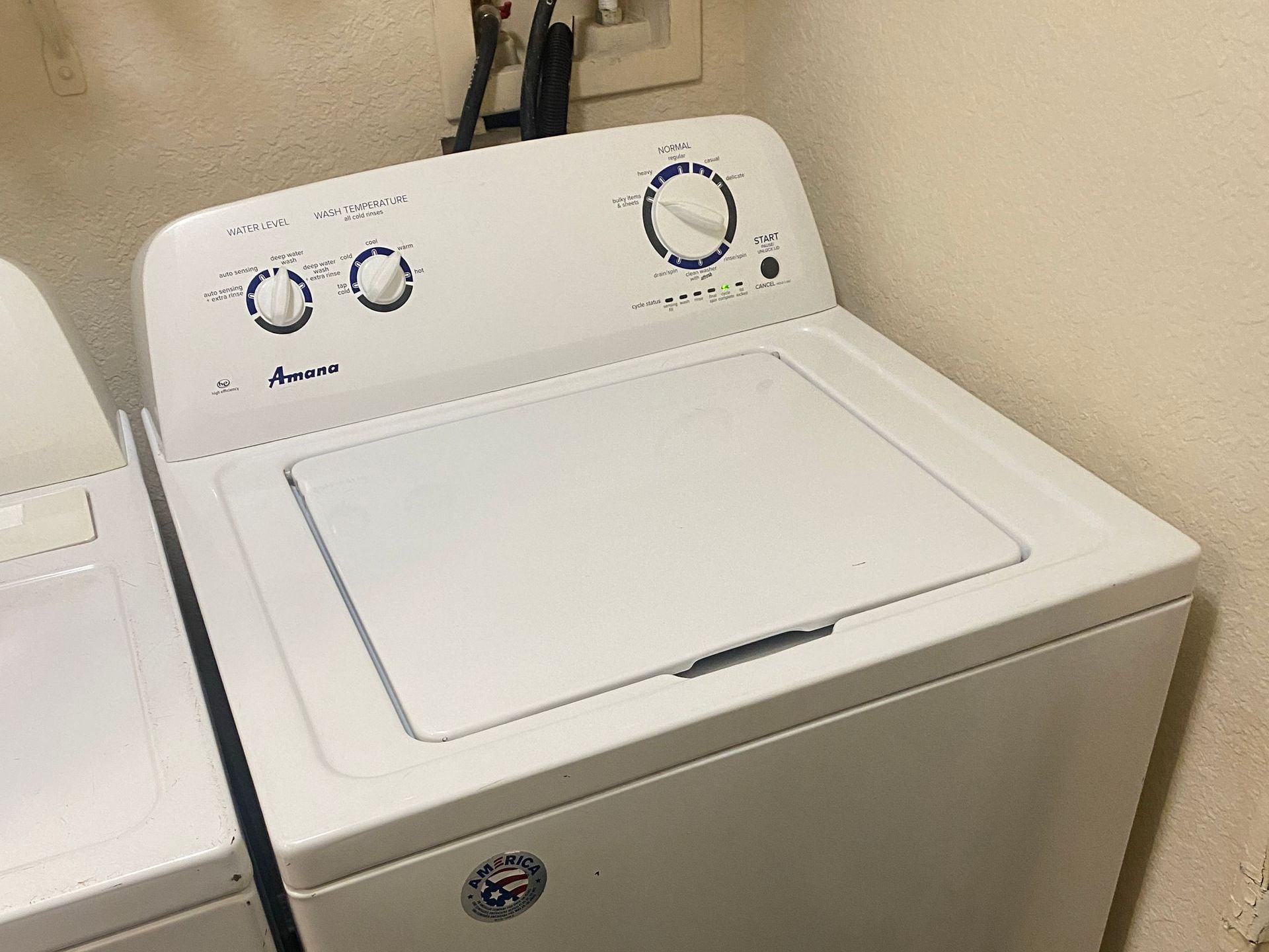 White top-load washing machine with control panel and closed lid in a laundry room.