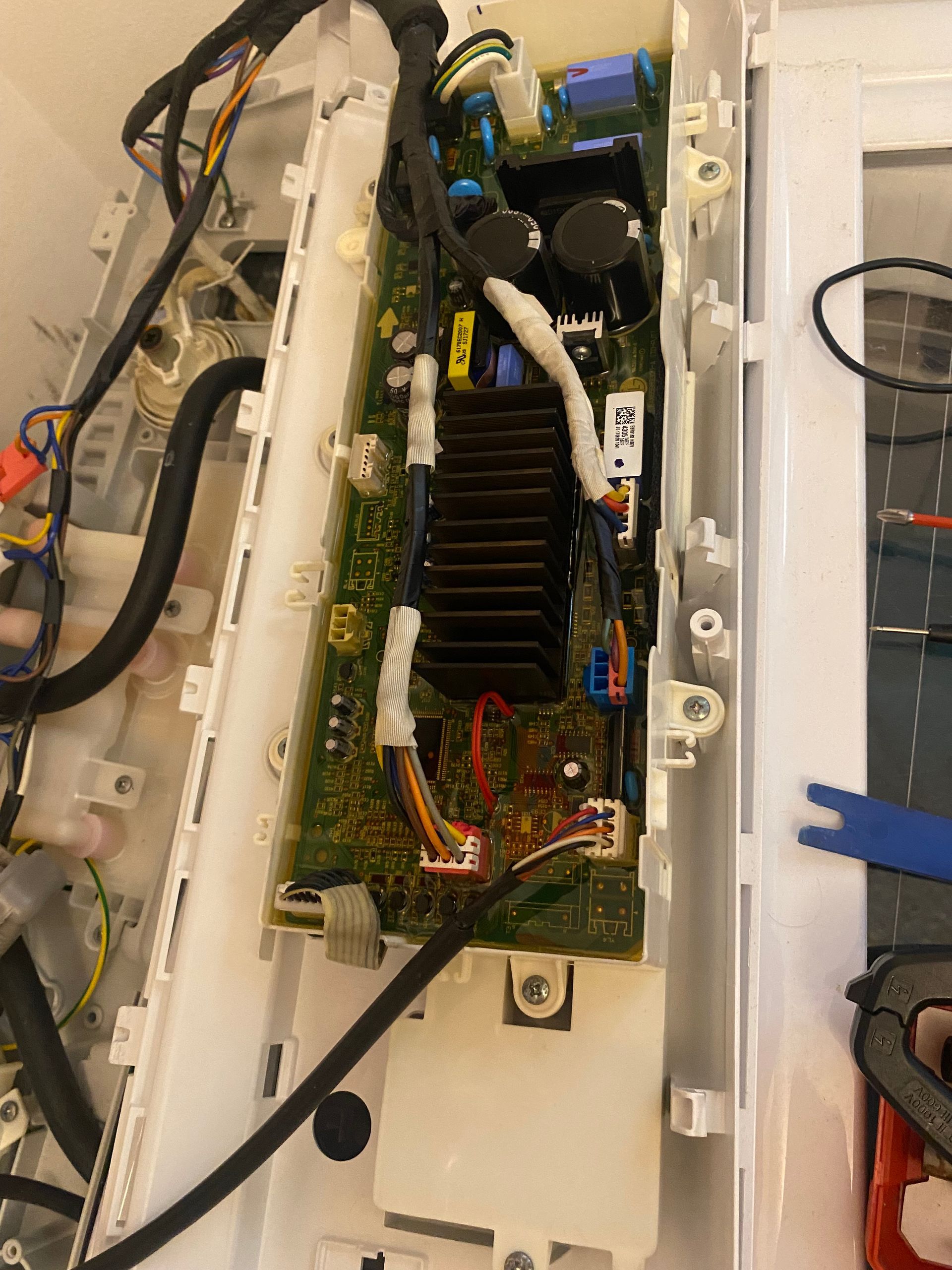 Washing machine control board. Green circuit board with wires, black heatsink, inside white plastic housing.
