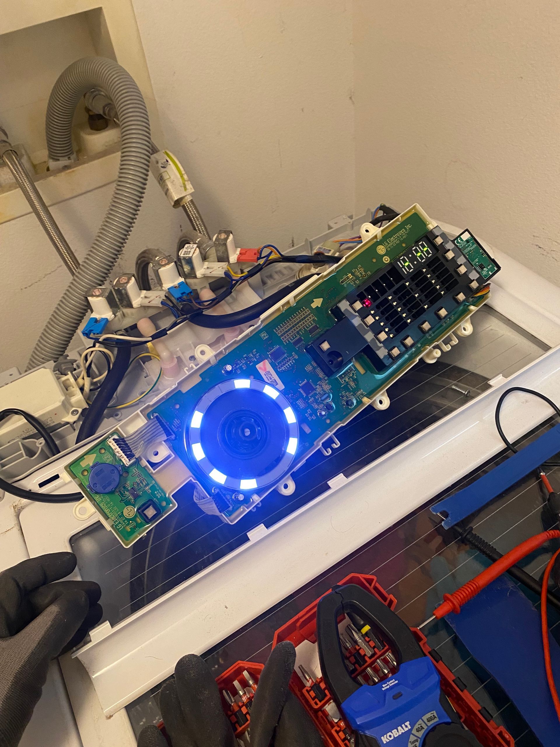 Washing machine control panel illuminated with blue light, open for repair.