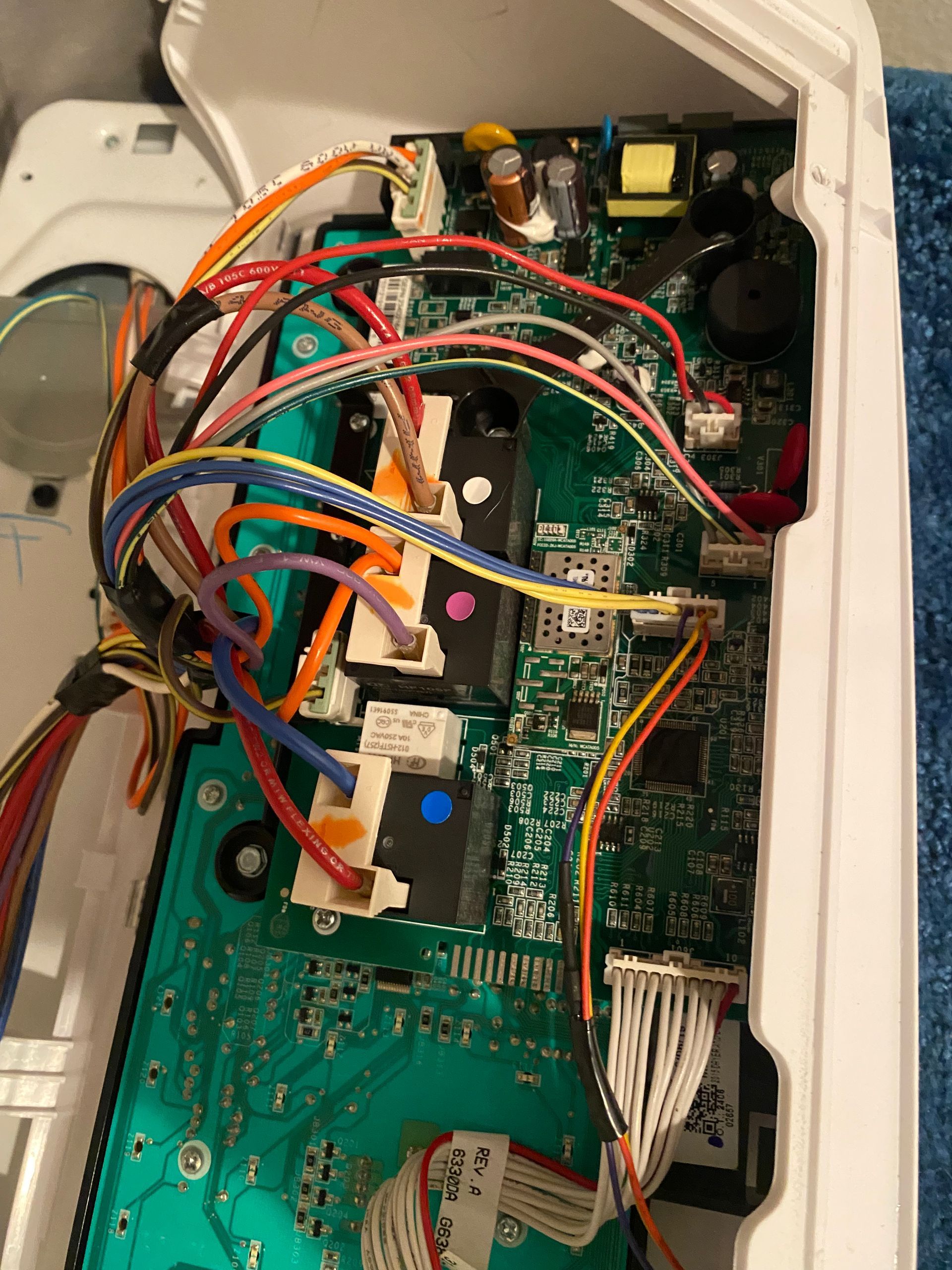 Internal view of a circuit board with multicolored wires and components inside a white appliance casing.