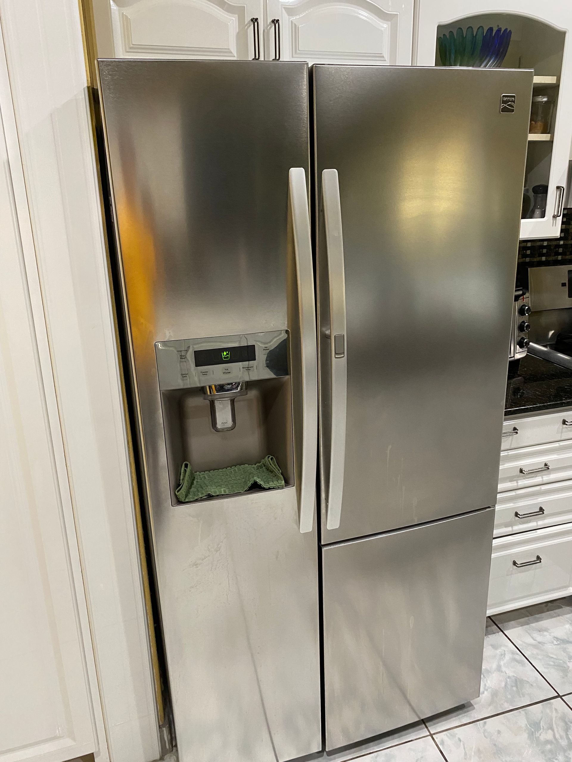 Stainless steel Kenmore side-by-side refrigerator in a kitchen with white cabinets.
