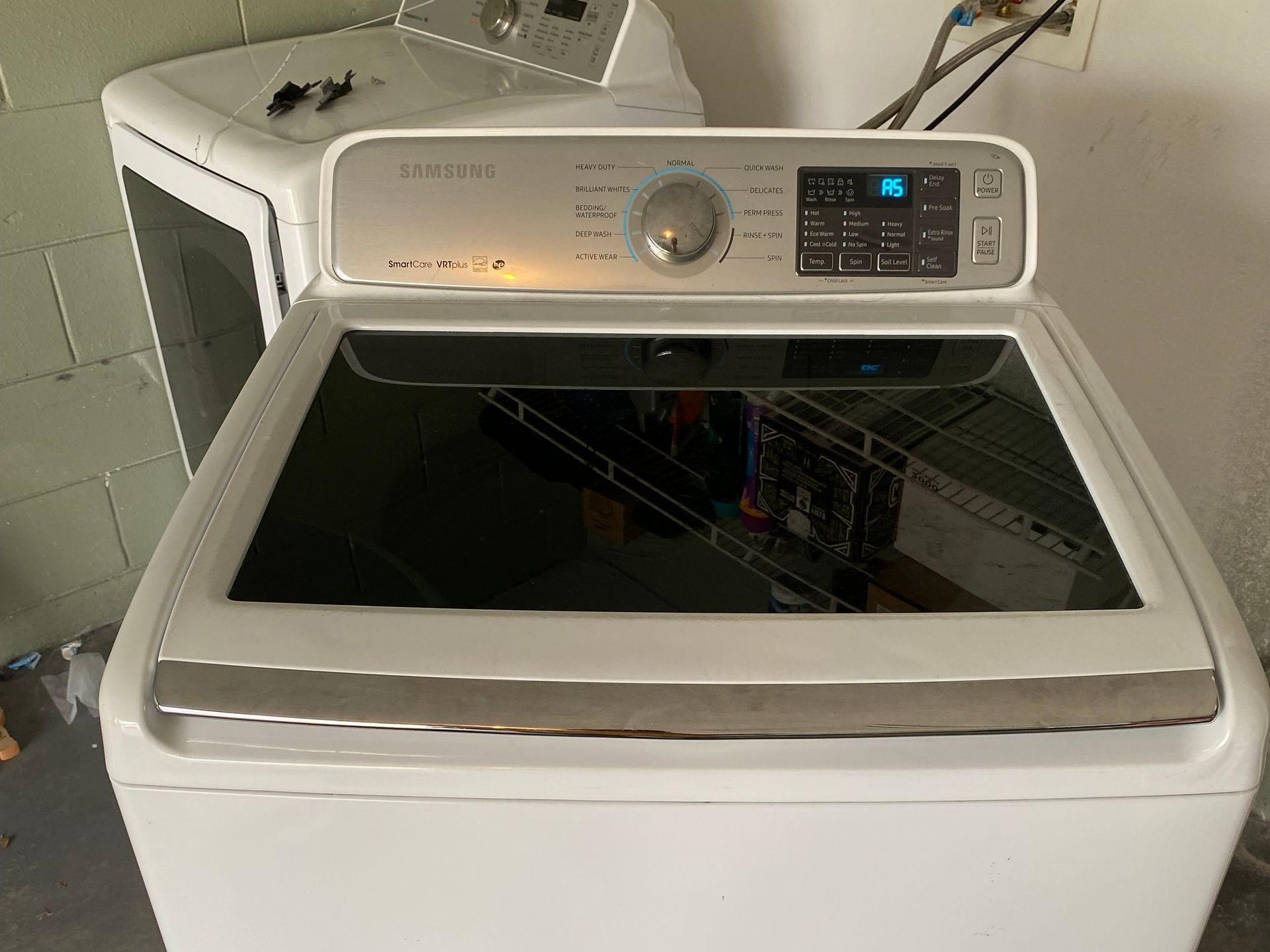White Samsung top-load washing machine with a glass lid, next to a similar white appliance.