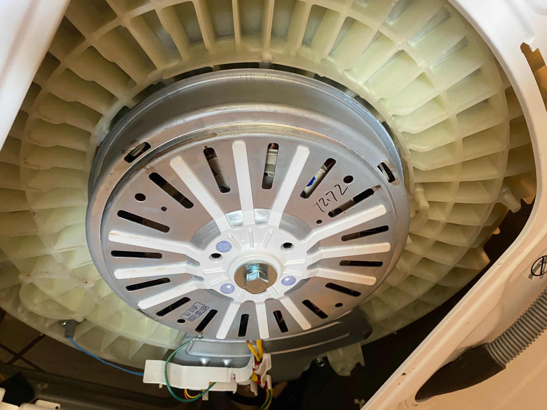 Inside of a washing machine; motor and pulley assembly. Beige and gray components.