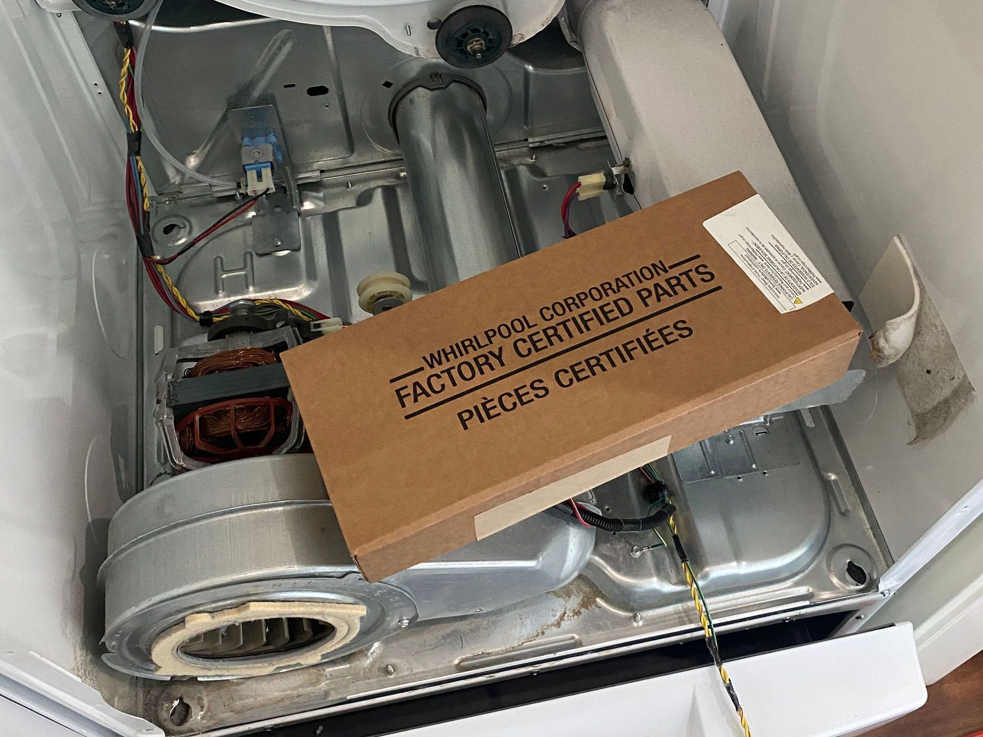 Inside of a dryer with a Whirlpool parts box. The dryer's components and a new box are visible.