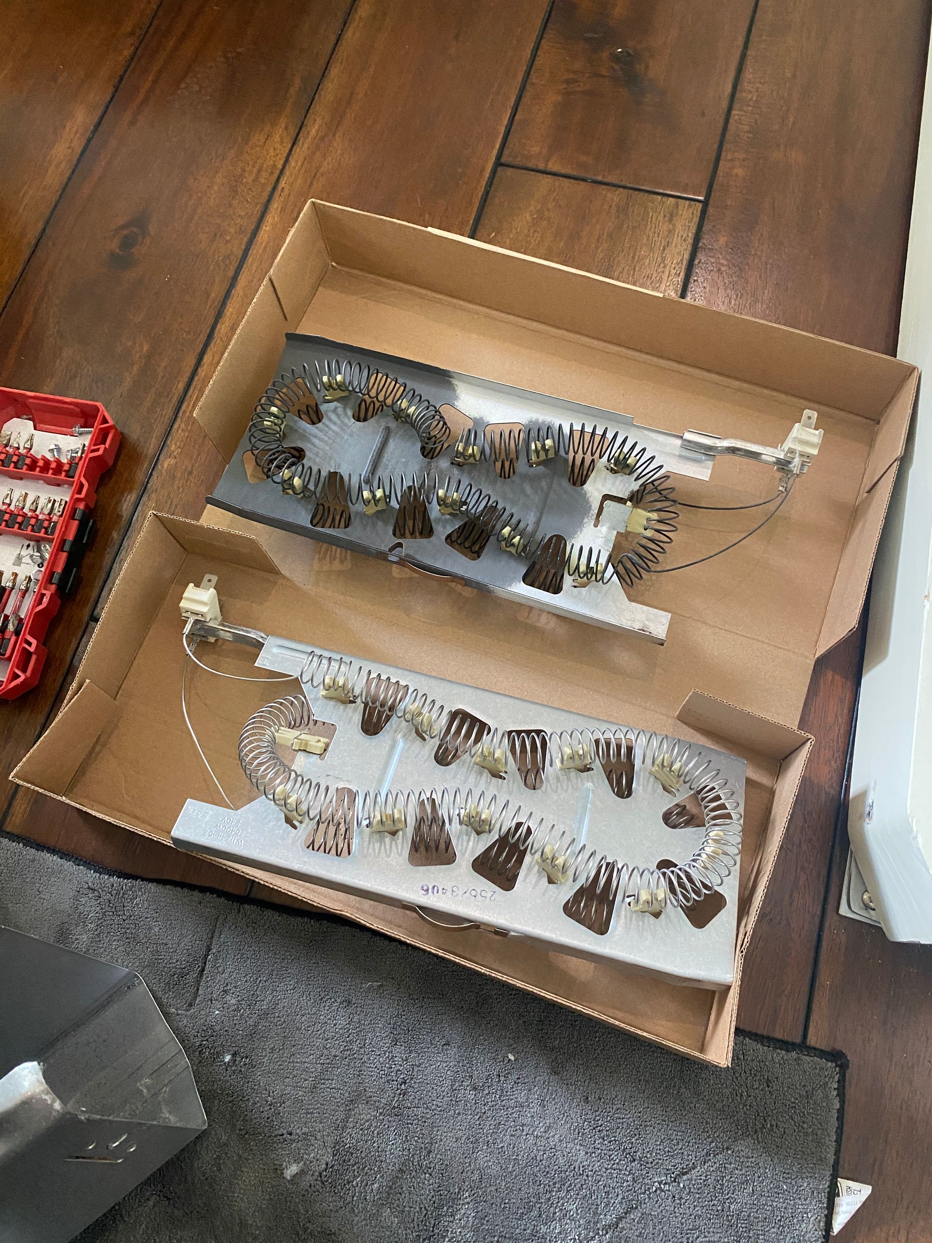 Two electric heater coils in a cardboard box on a wooden floor.