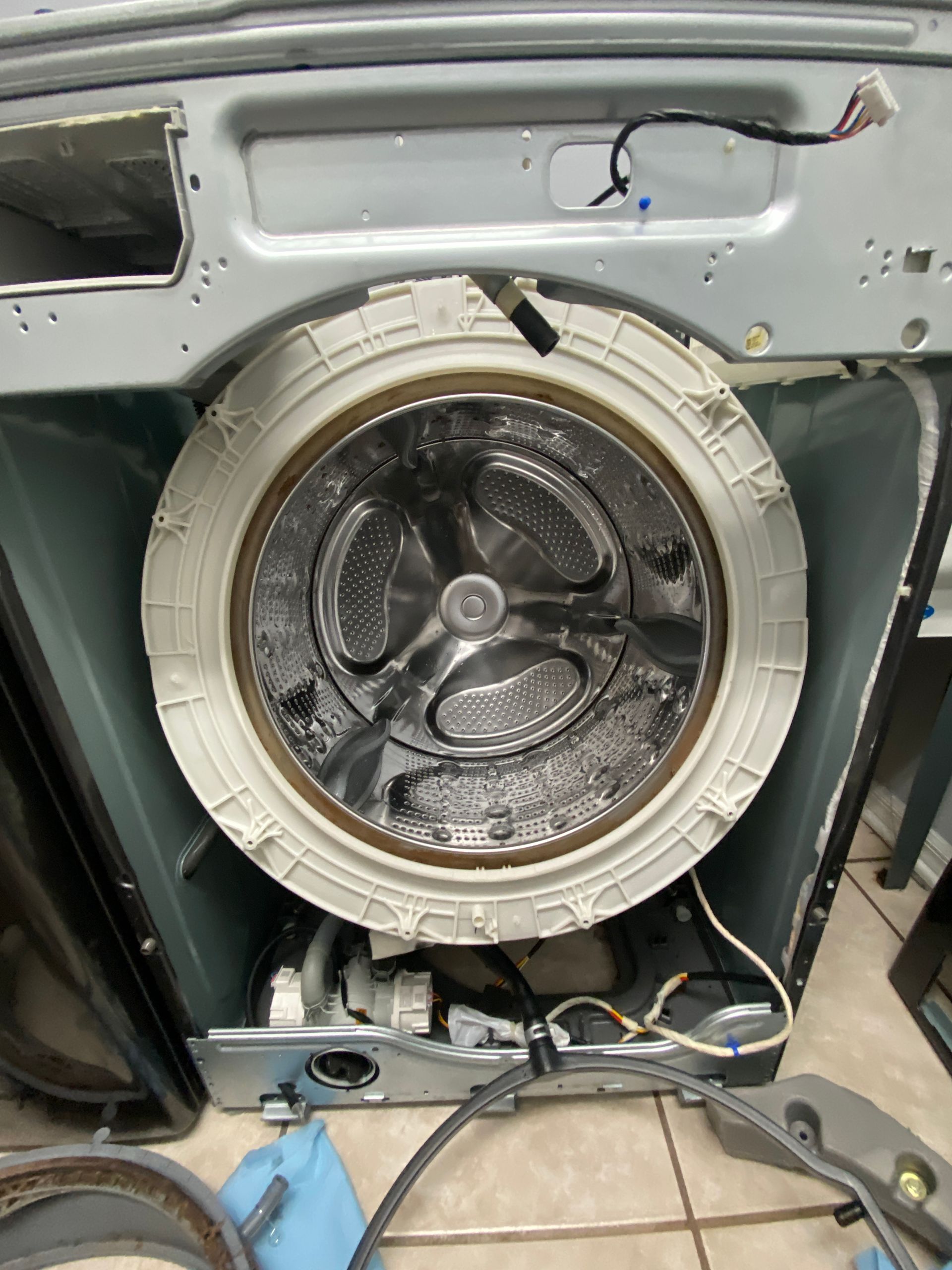 Washing machine interior with the drum visible, disassembled for repair. Gray and white components.