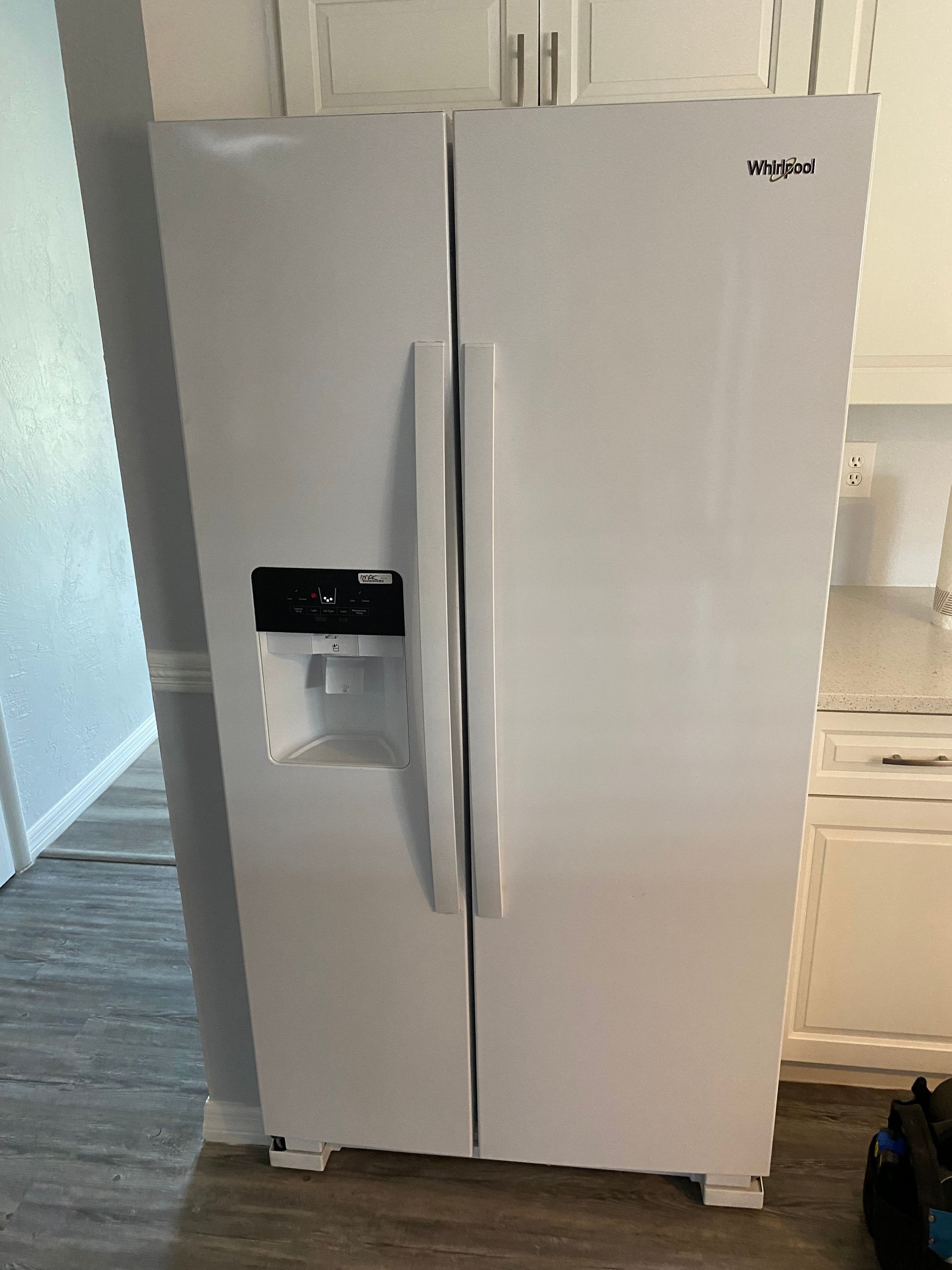 White Whirlpool side-by-side refrigerator in a kitchen with a water dispenser on the front.