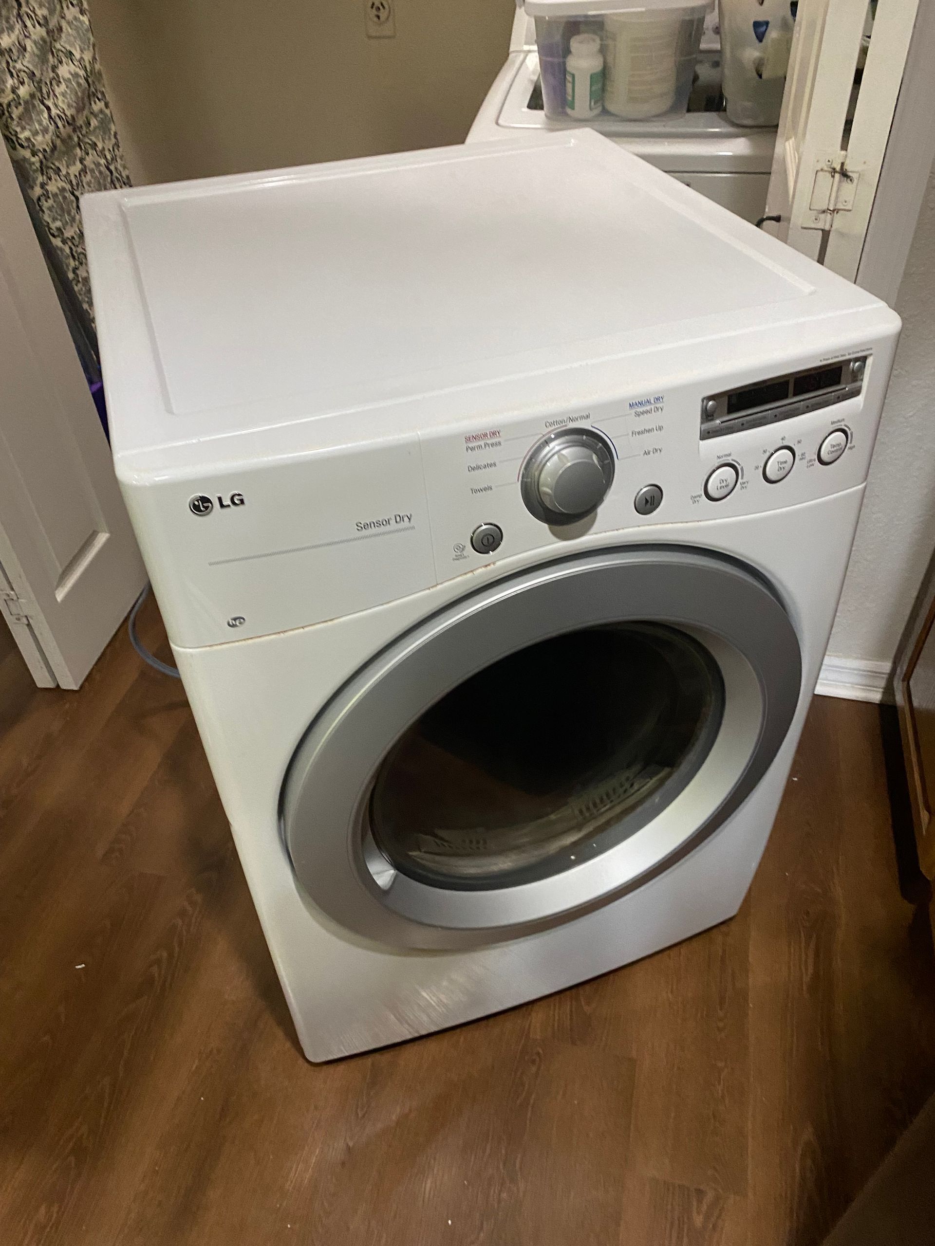 White LG dryer on a wooden floor in a laundry room.