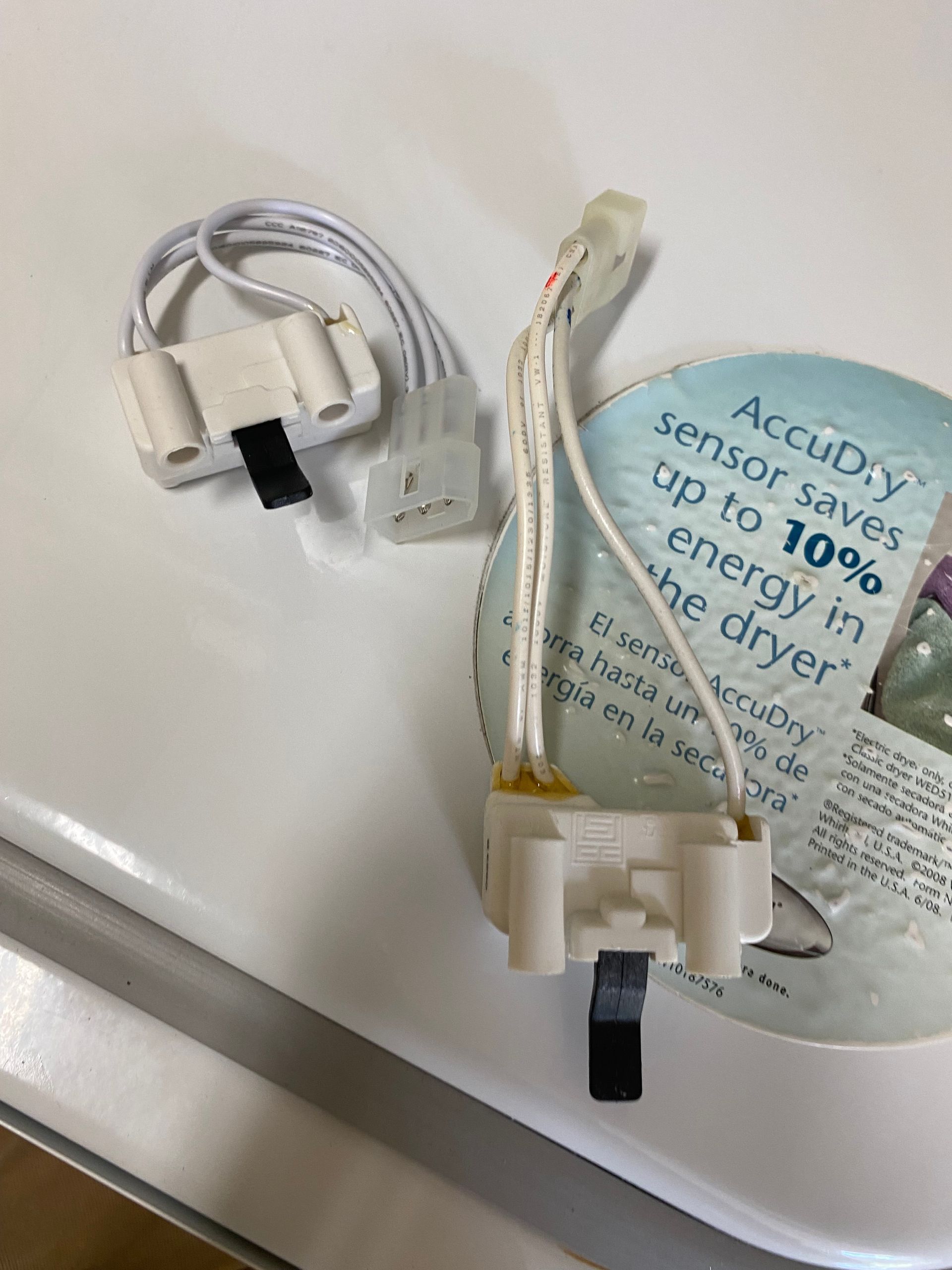 Two white dryer sensors with white wires, laying on top of a white dryer.