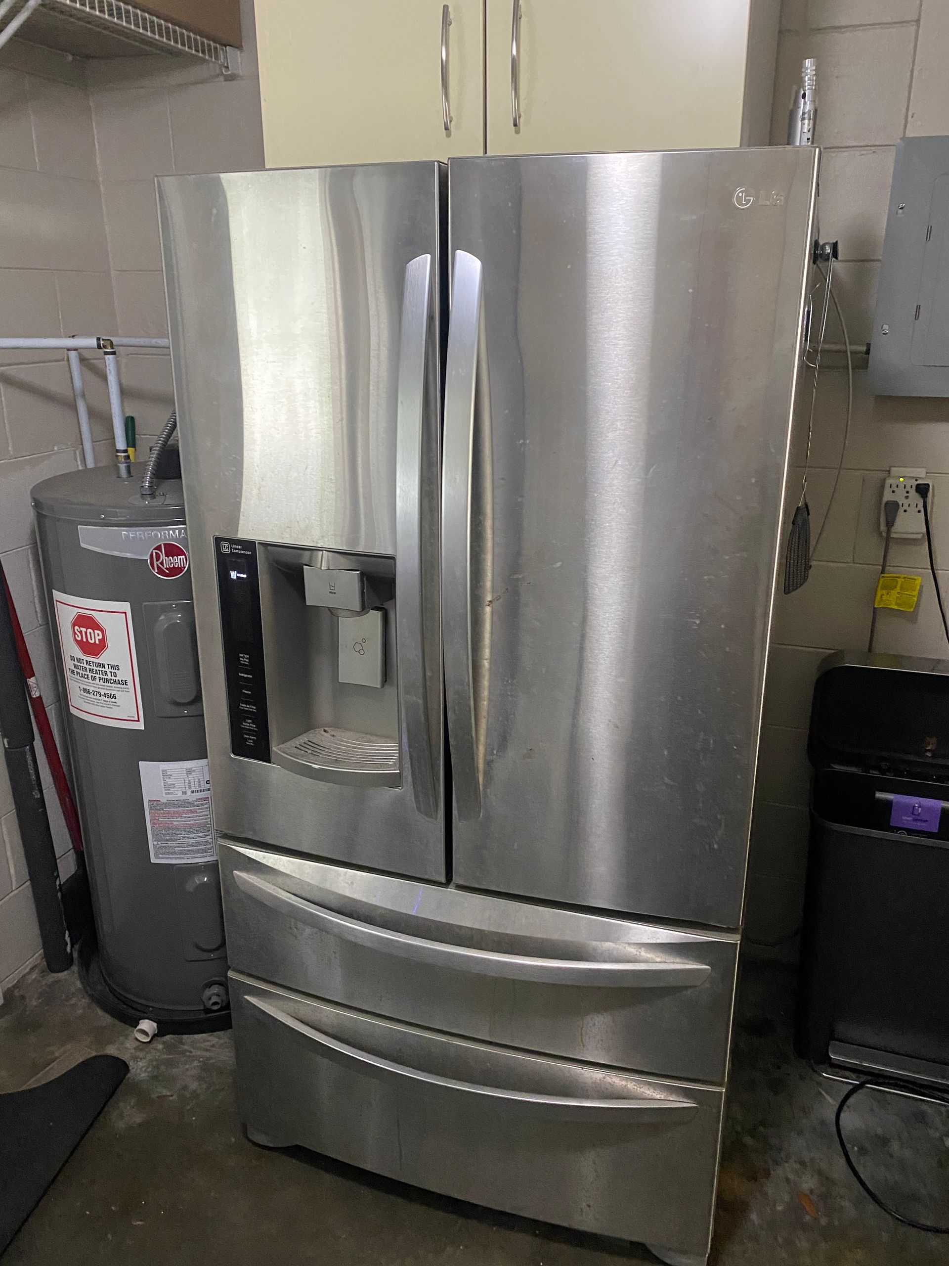 Stainless steel LG refrigerator with water dispenser in a utility room next to a water heater.