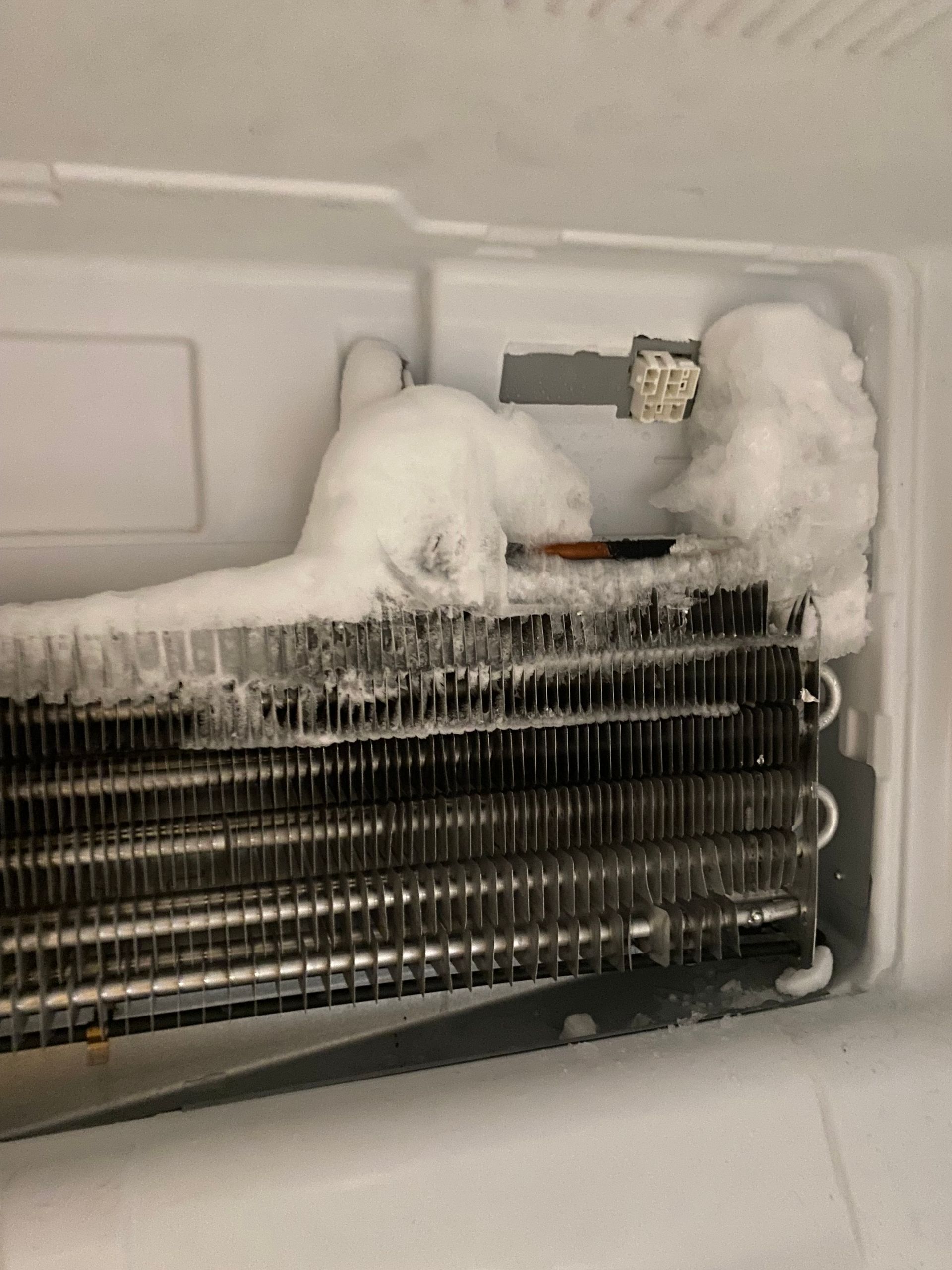 Inside a refrigerator freezer: frost buildup on the cooling coils, obscuring the fan.