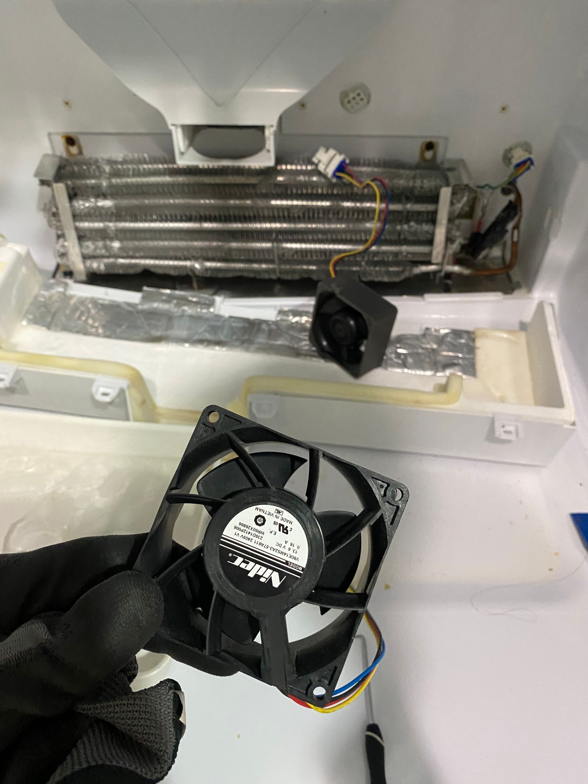 Refrigerator repair: A person holds a black fan with a disconnected fan inside the appliance. 