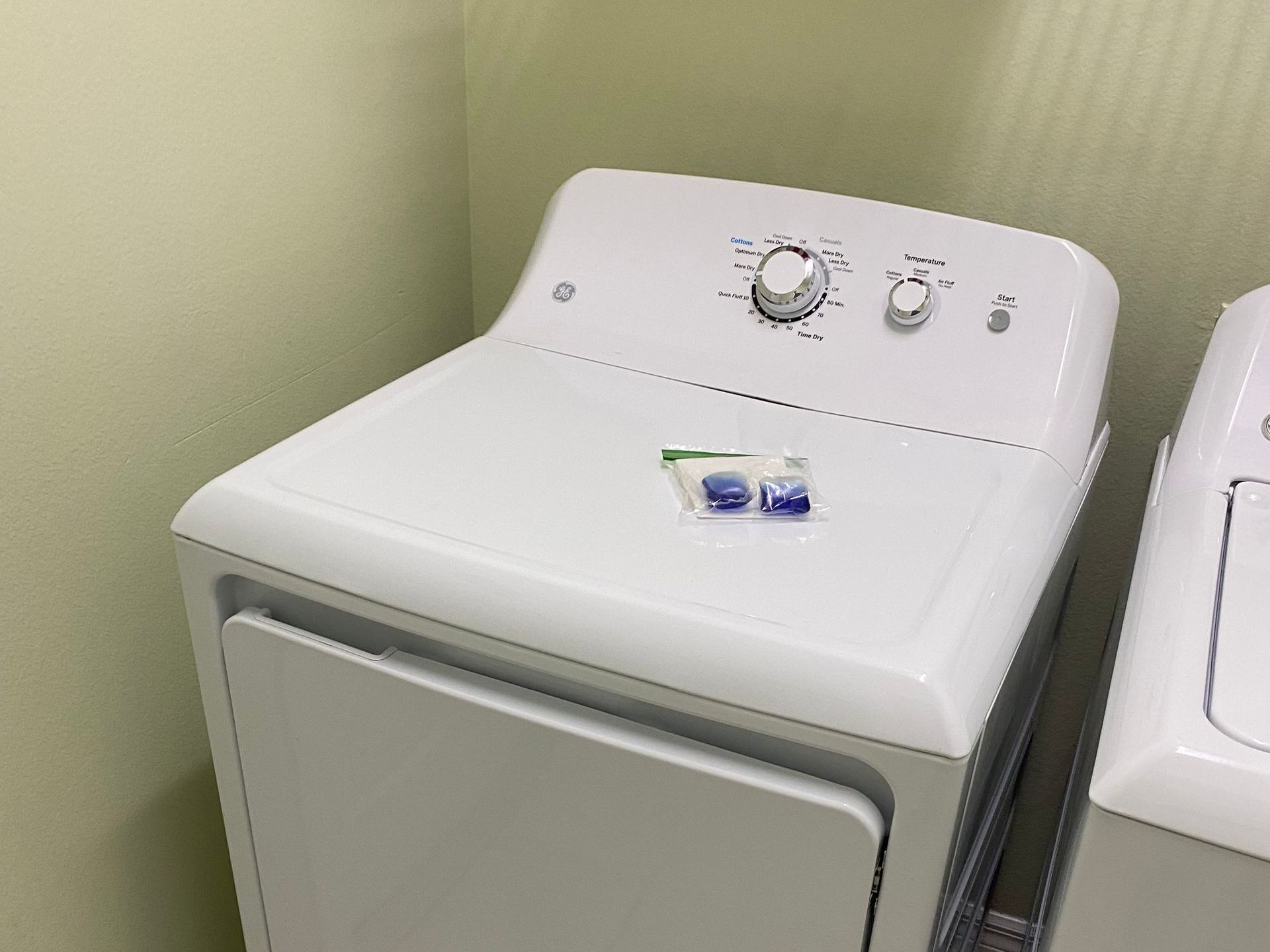 White dryer with control knobs and laundry detergent pods on top.