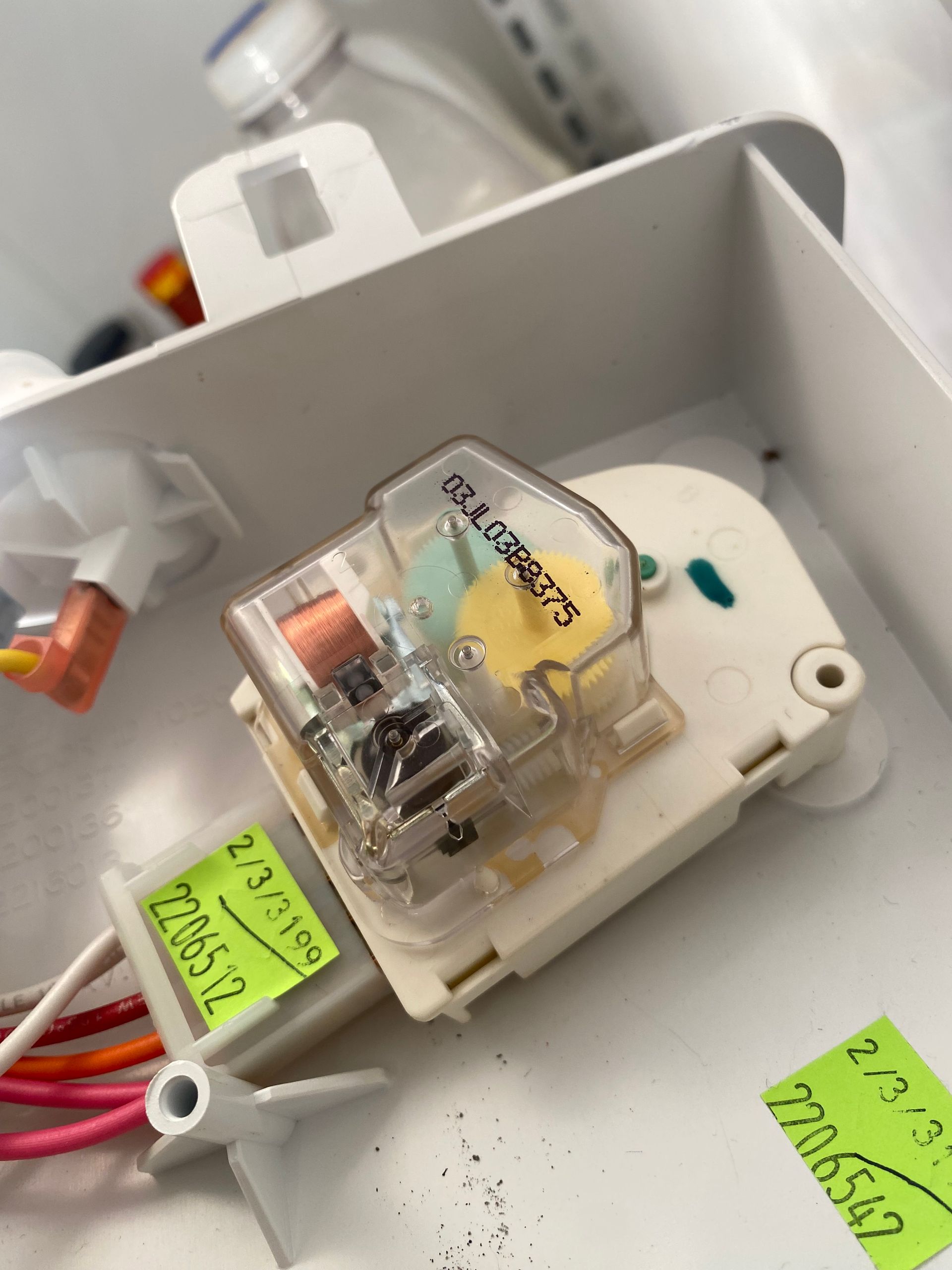 Refrigerator defrost timer. Beige plastic component with electrical wires and labels.