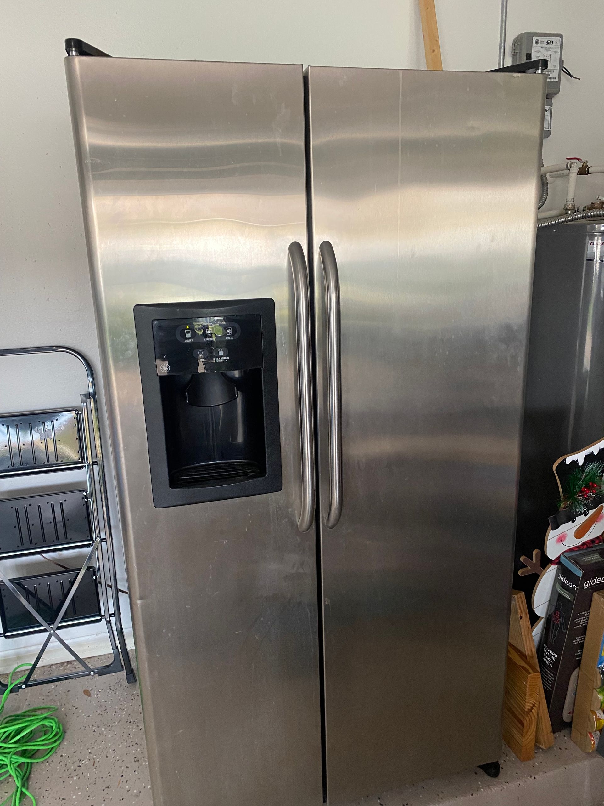 Stainless steel side-by-side refrigerator with water/ice dispenser in a garage.