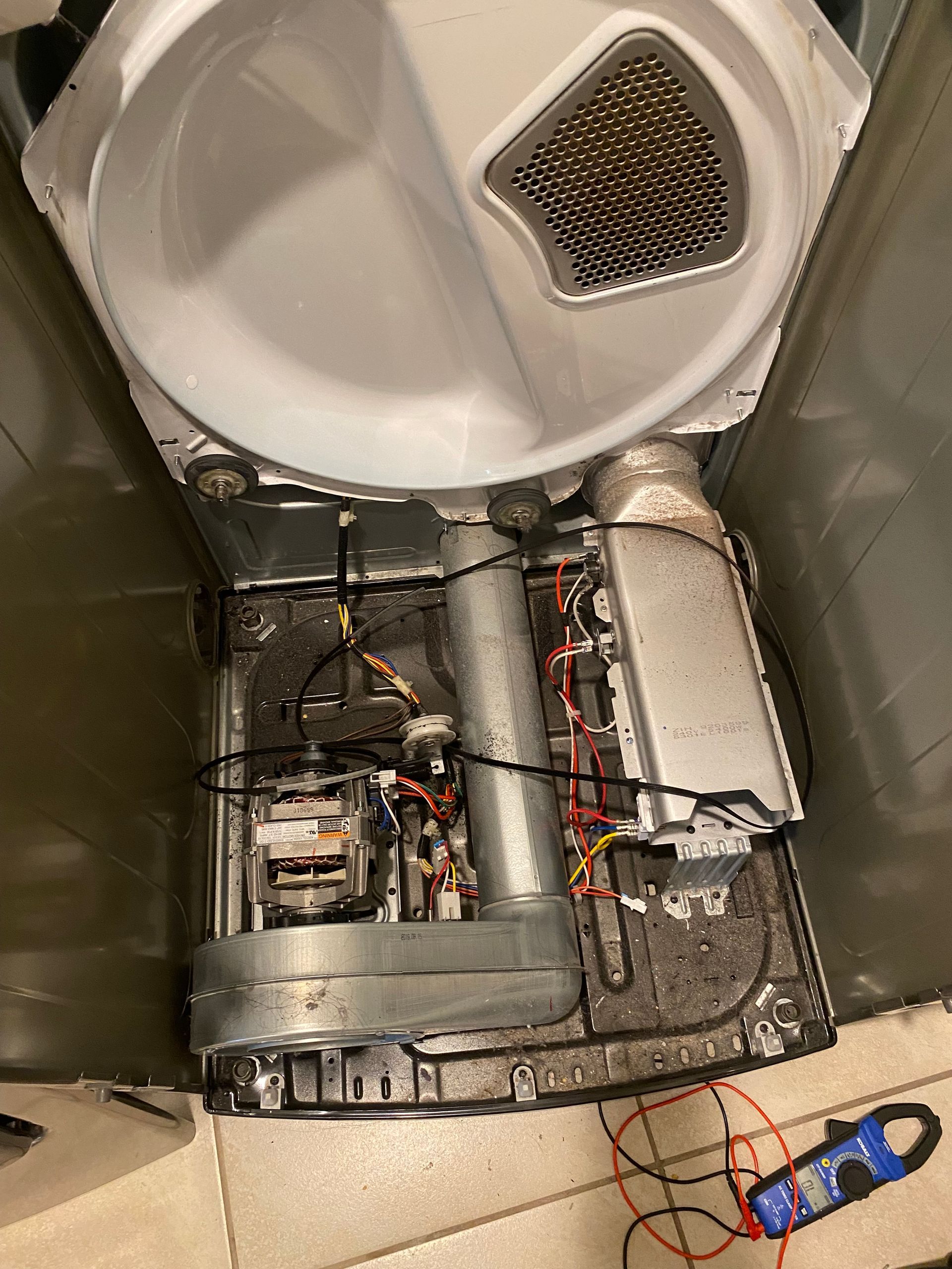 Interior of a dryer with components exposed; a technician may be inspecting the motor and heating element.
