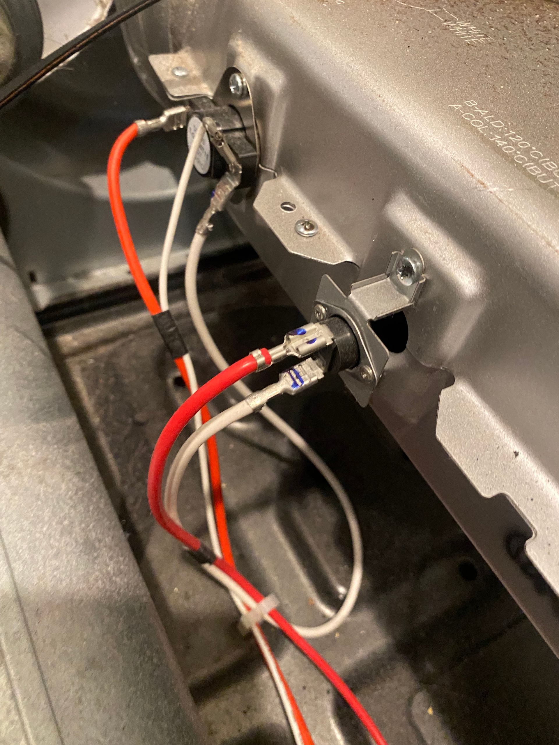 Close-up of dryer components; orange and white wires connected to a thermal fuse and thermostat on a metal housing.