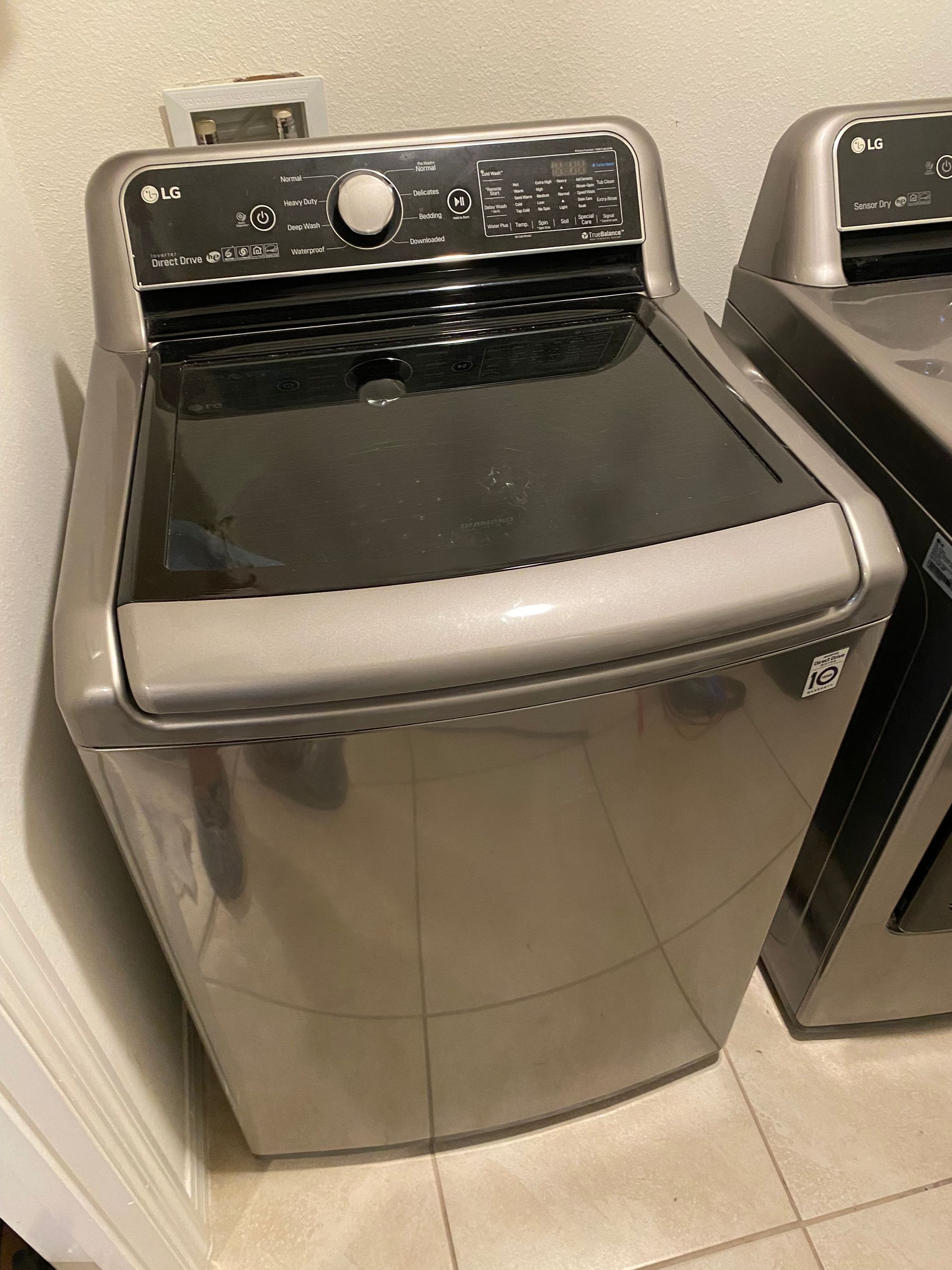 LG top-load washing machine with dark gray lid in a laundry room.