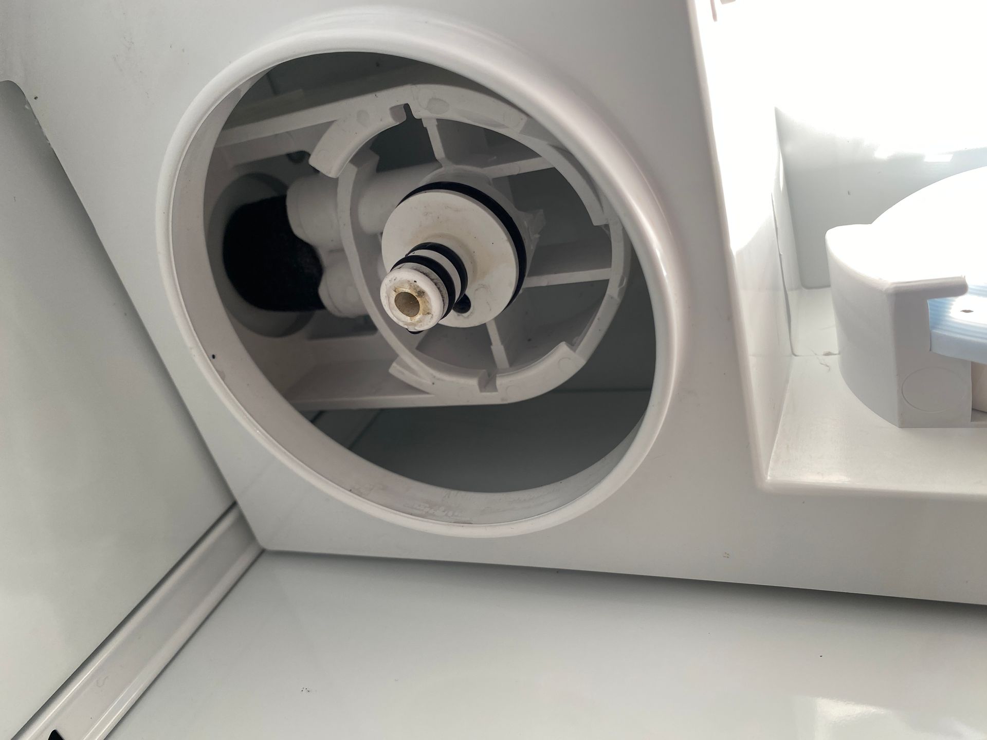 White refrigerator water filter housing with central fitting.
