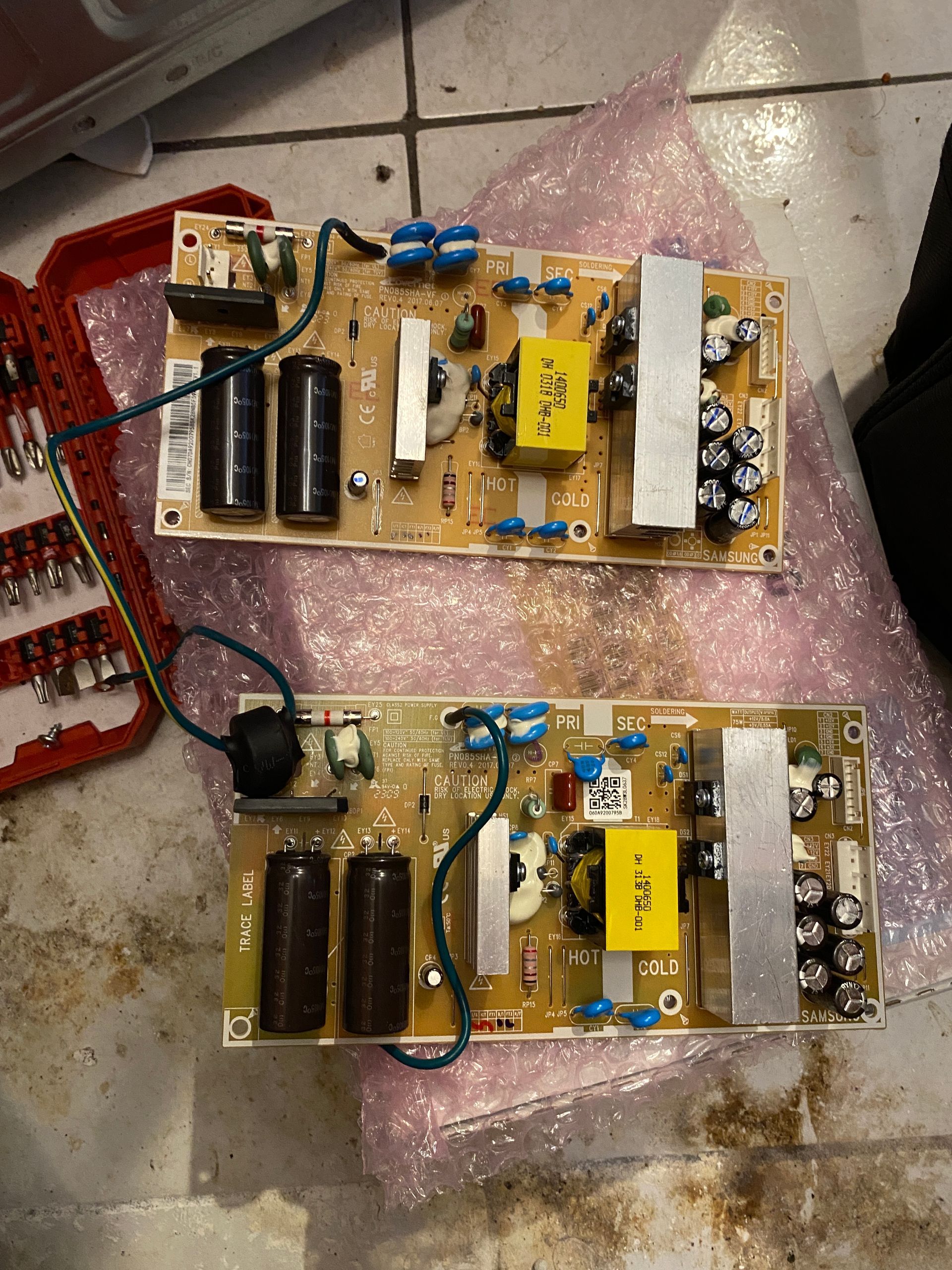 Two circuit boards with various electronic components are laying on a surface with a toolbox nearby.