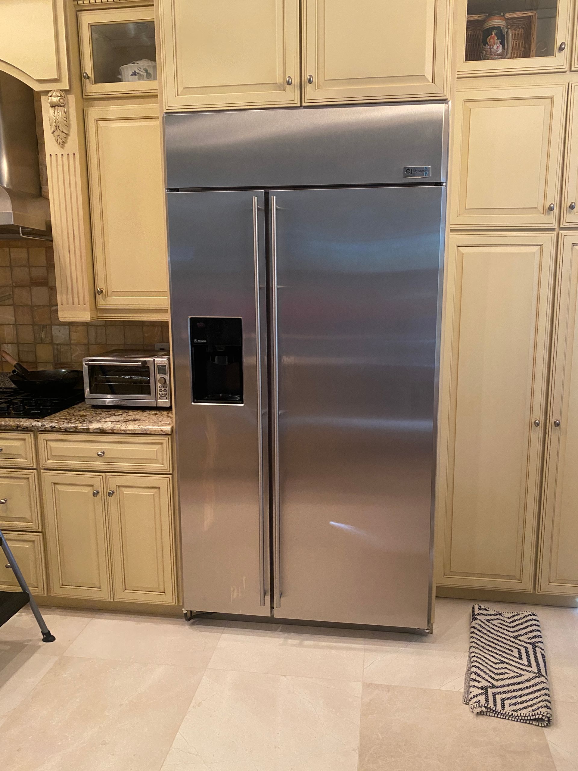 Stainless steel side-by-side refrigerator in a kitchen with cream-colored cabinets and a toaster.