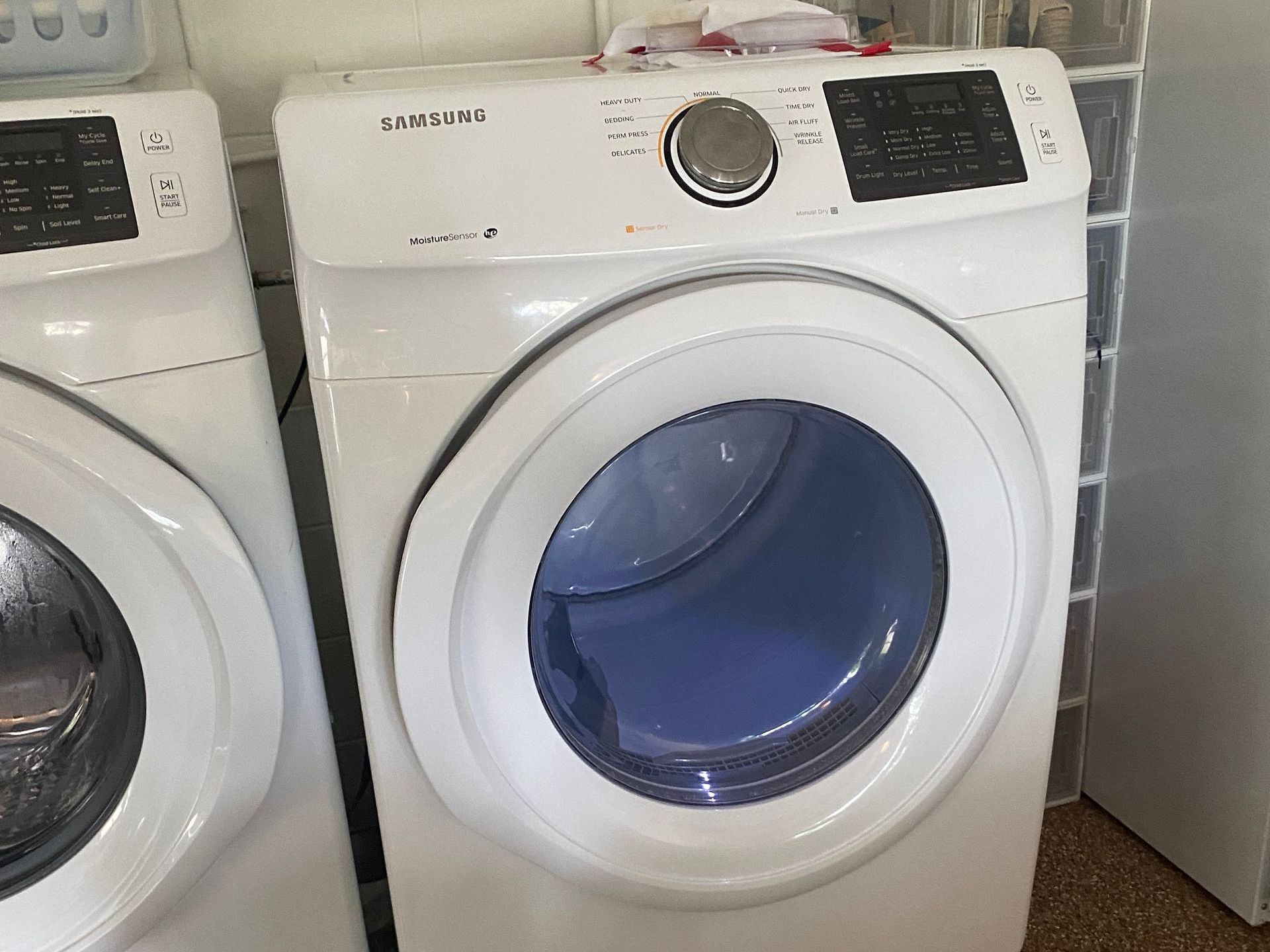 White Samsung dryer with a blue interior drum next to a similar washing machine.