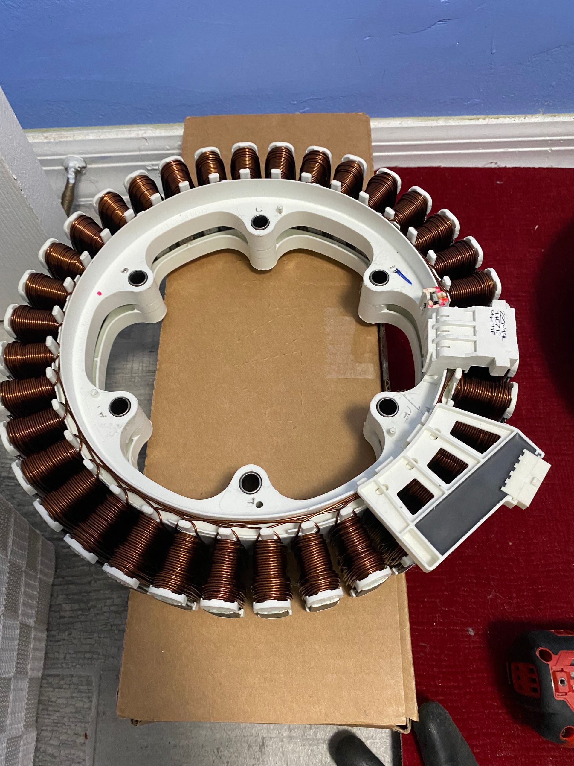 Circular stator with copper coils and white plastic frame, possibly from an appliance, resting on cardboard.