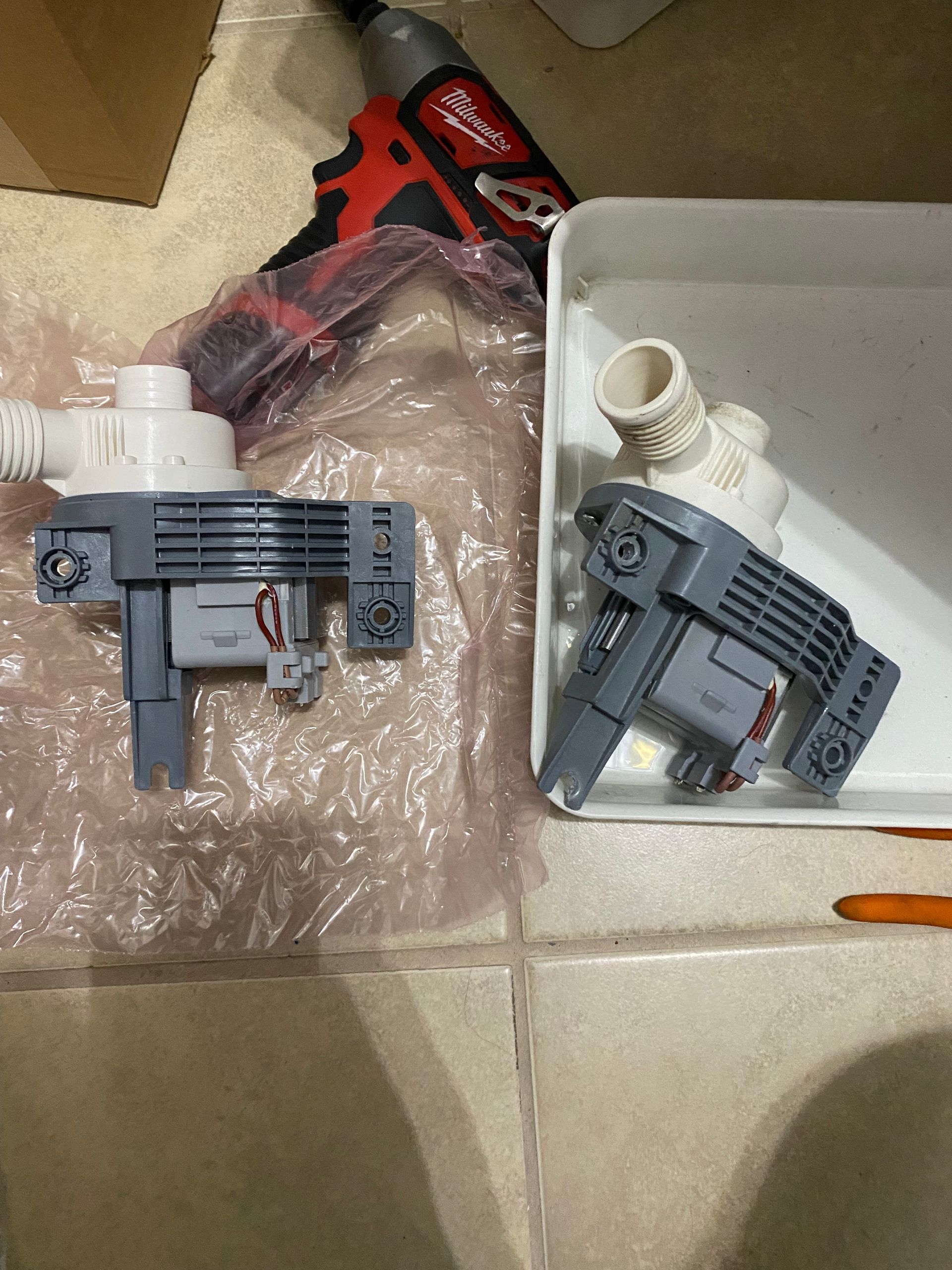 Two gray and white appliance pumps with attached electrical components, lying on a surface.