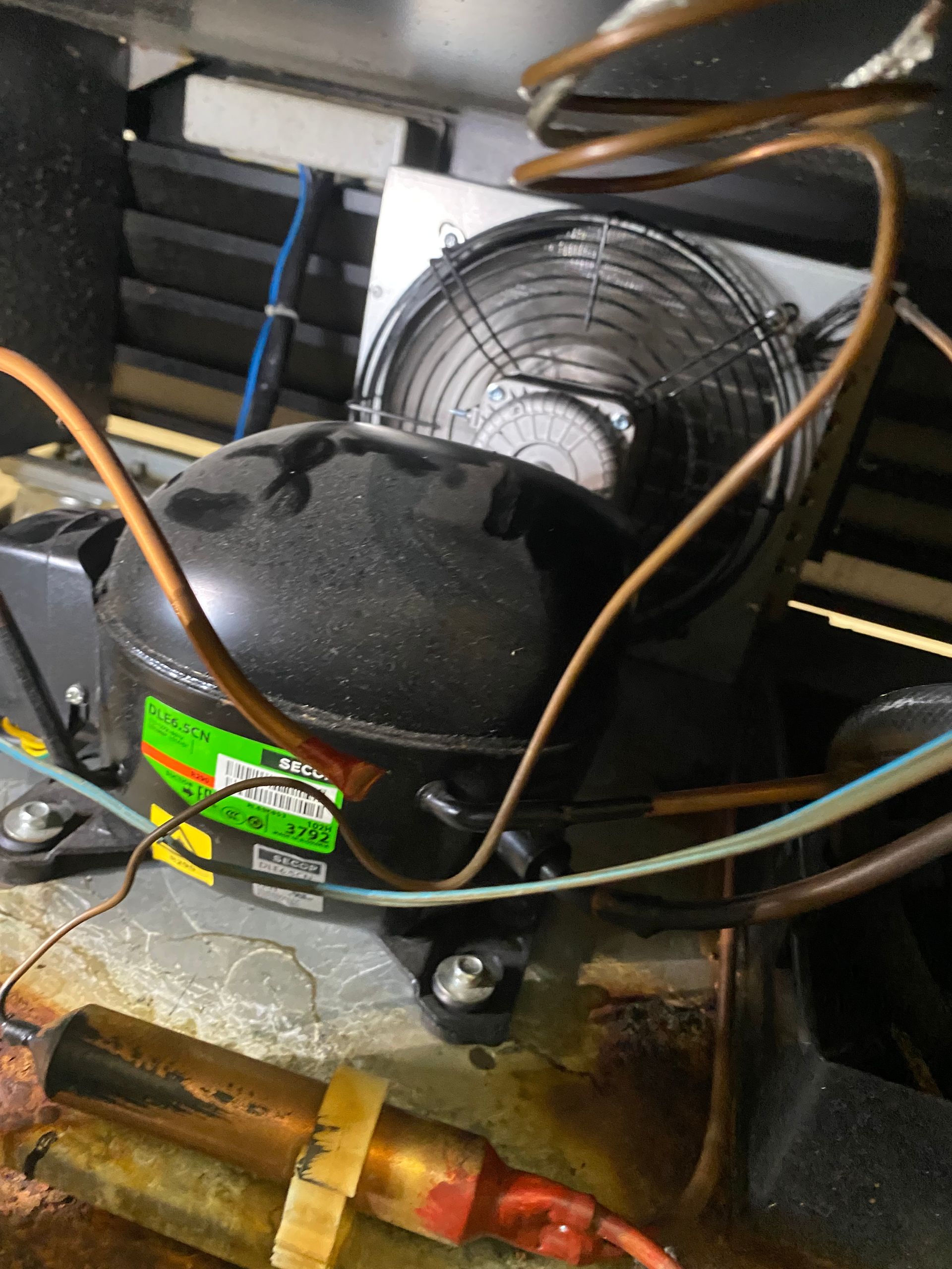 Black compressor with copper tubing and a fan in an appliance.