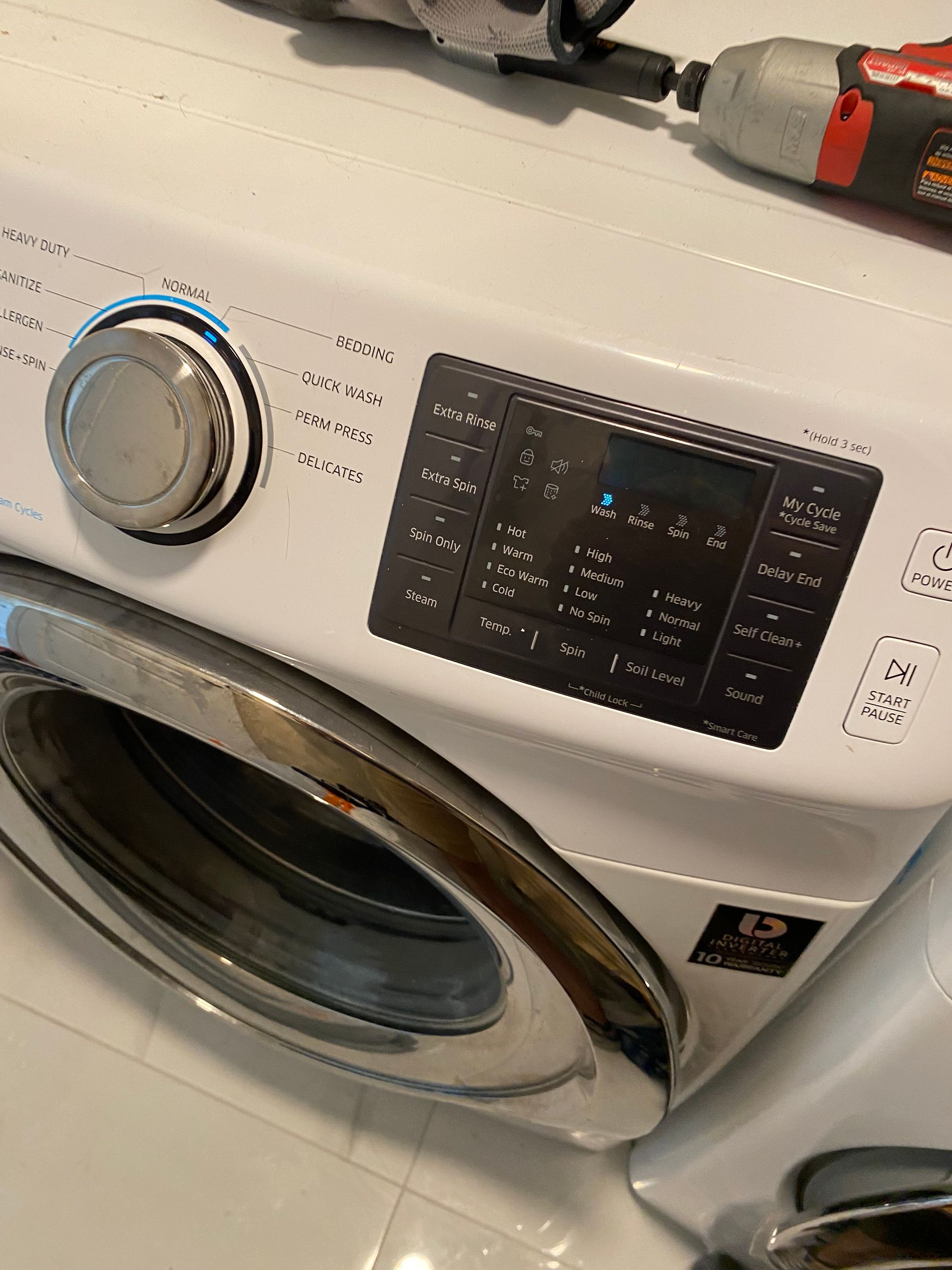 White Samsung washing machine with control panel and chrome door, tools on top.
