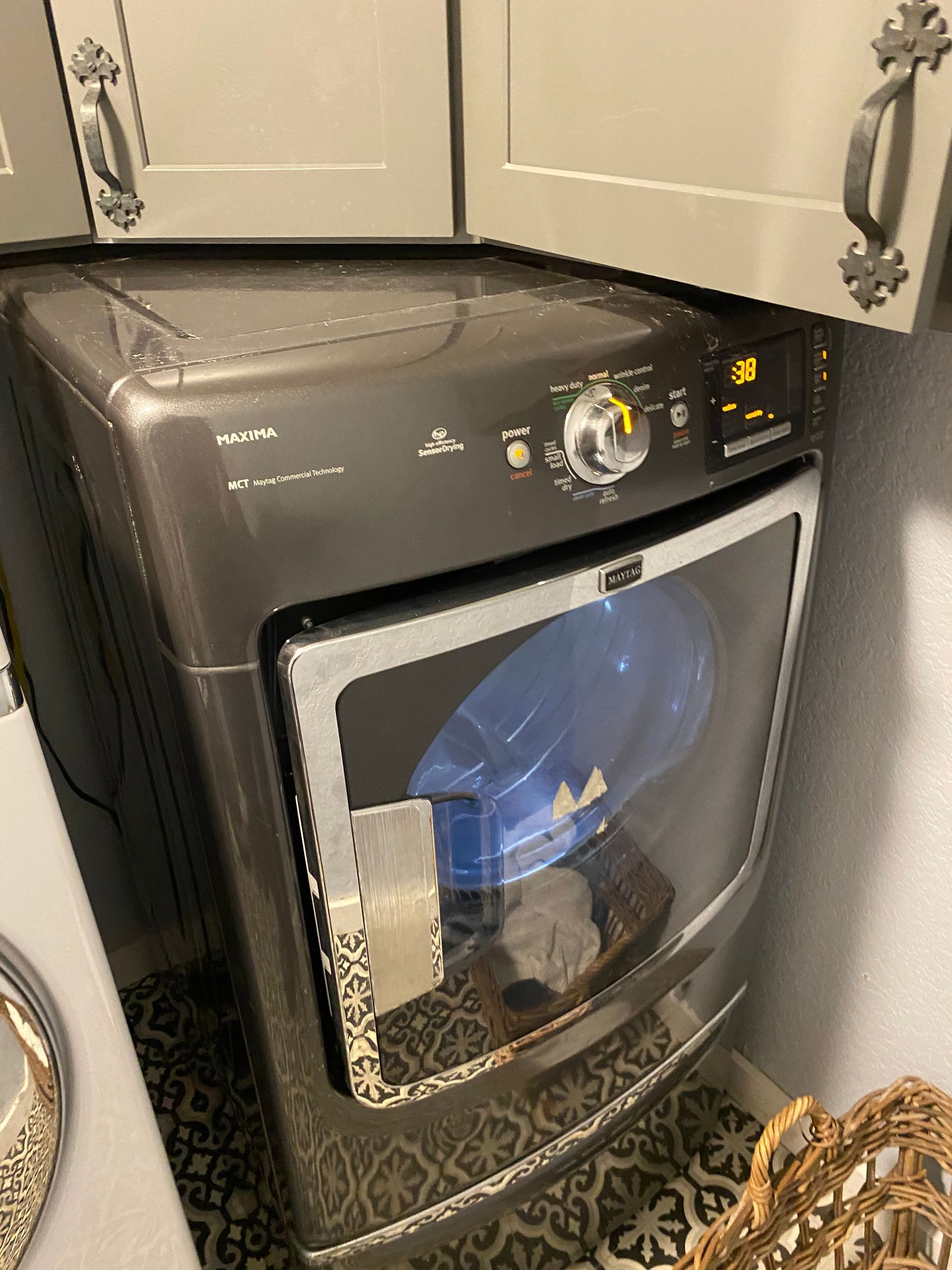Gray dryer with a glass door in a laundry room, beneath gray cabinets.