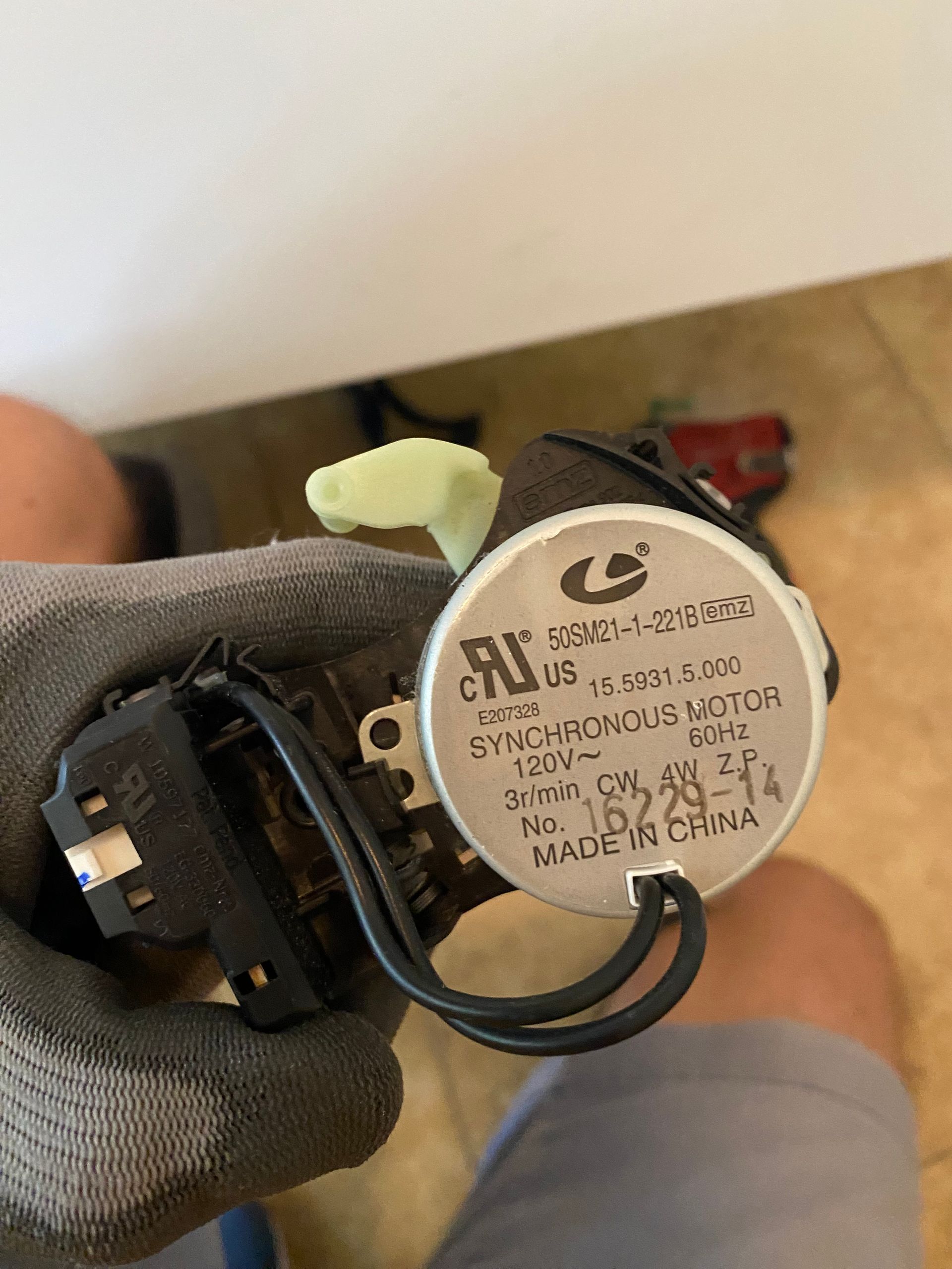 Synchronous motor, black wires, silver label, held by a person wearing a glove.