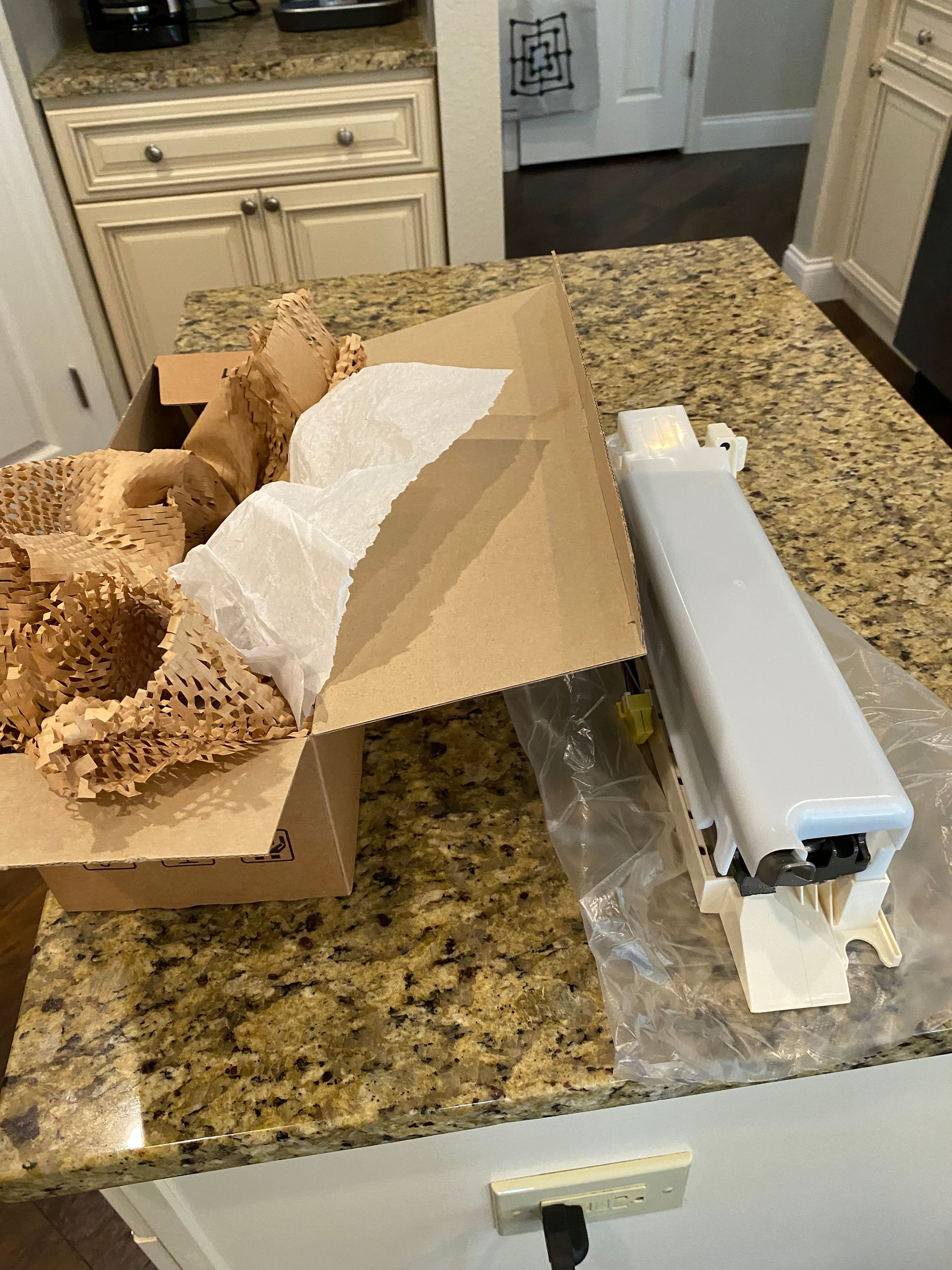 Open cardboard box and packaged object on a granite countertop in a kitchen.