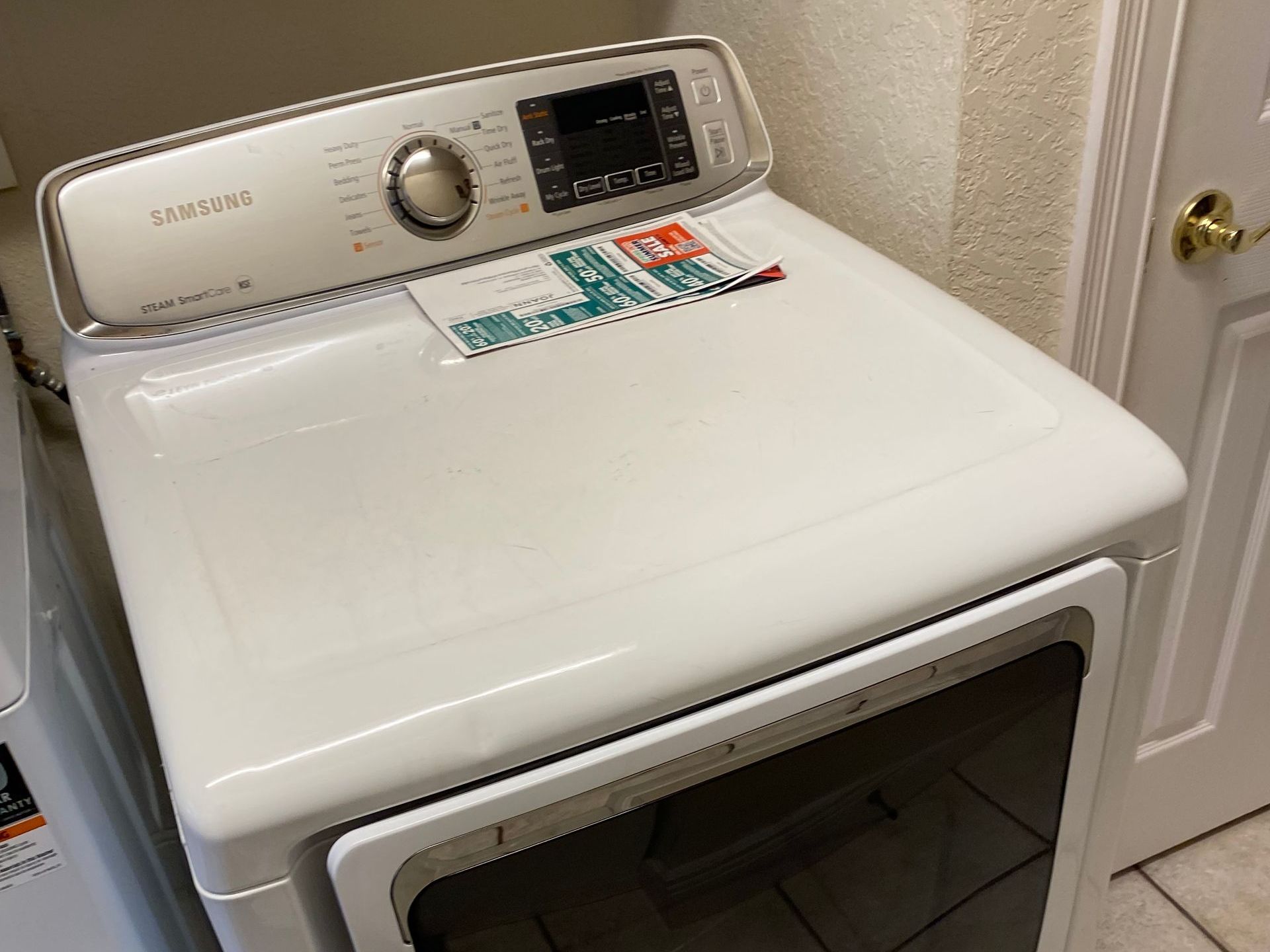White Samsung dryer in a laundry room, with control panel and open door.