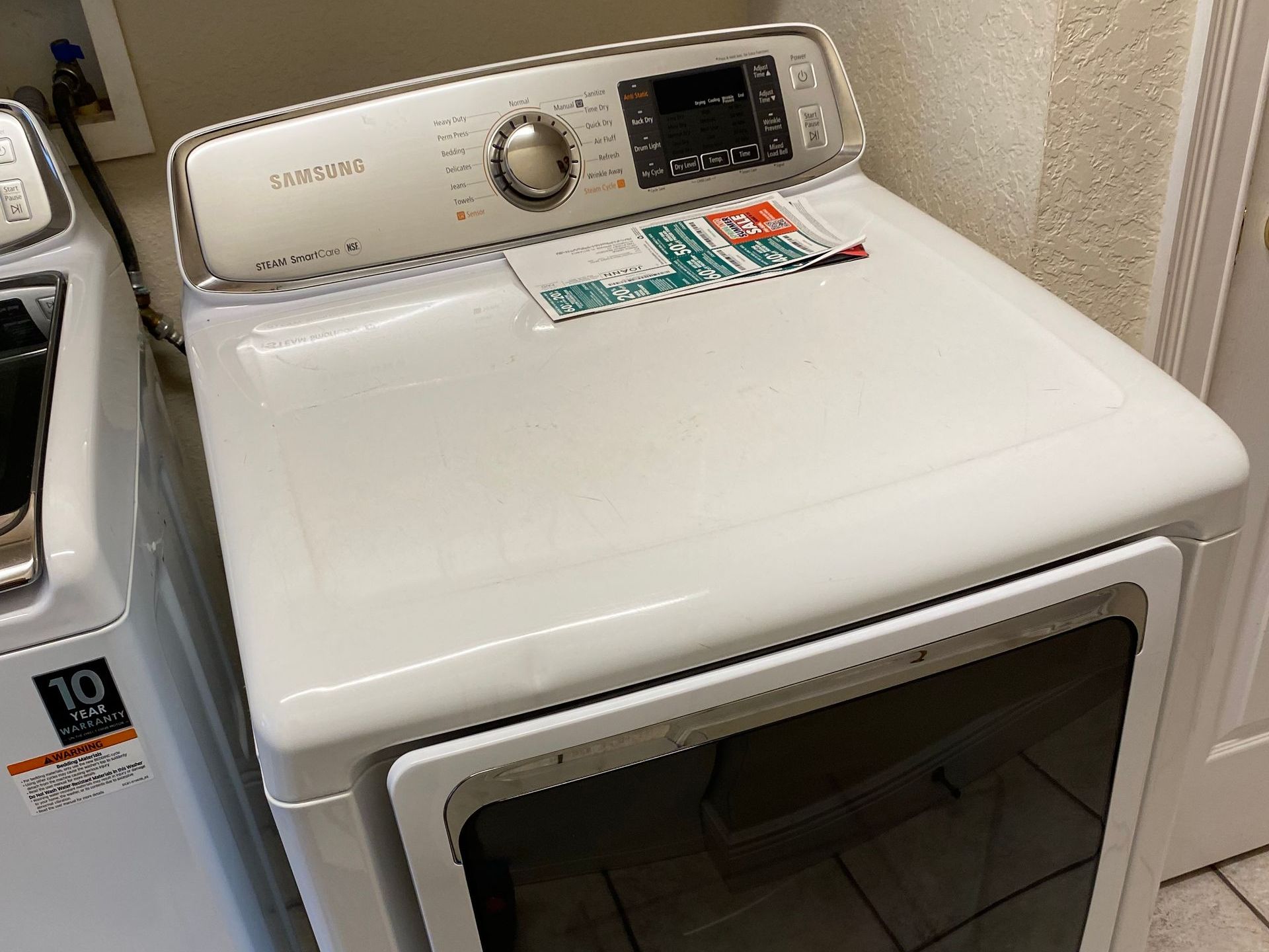 White Samsung dryer with an open door in a laundry room.