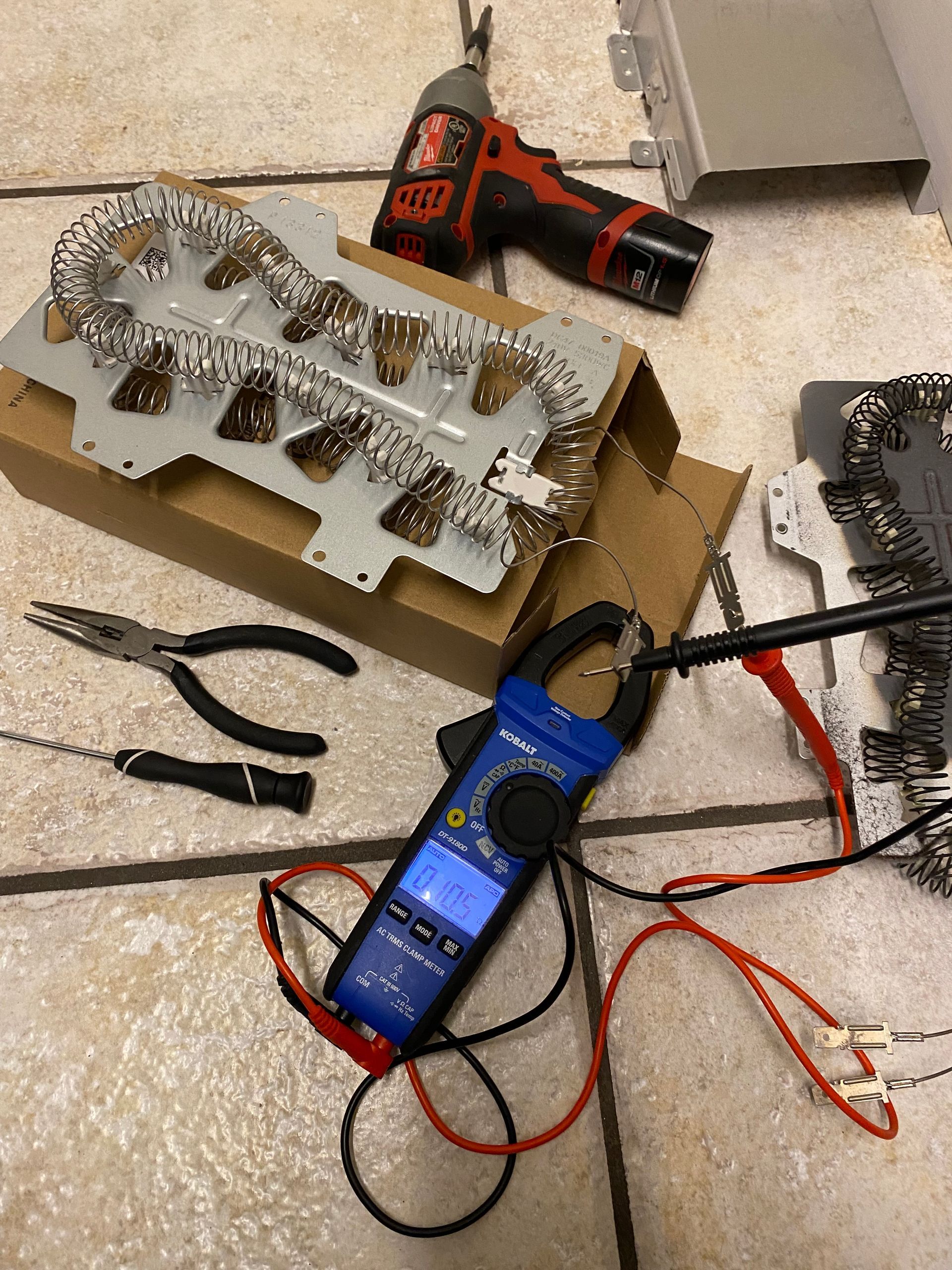 Dryer heating element and tools on a tiled floor with a multimeter measuring electrical resistance.