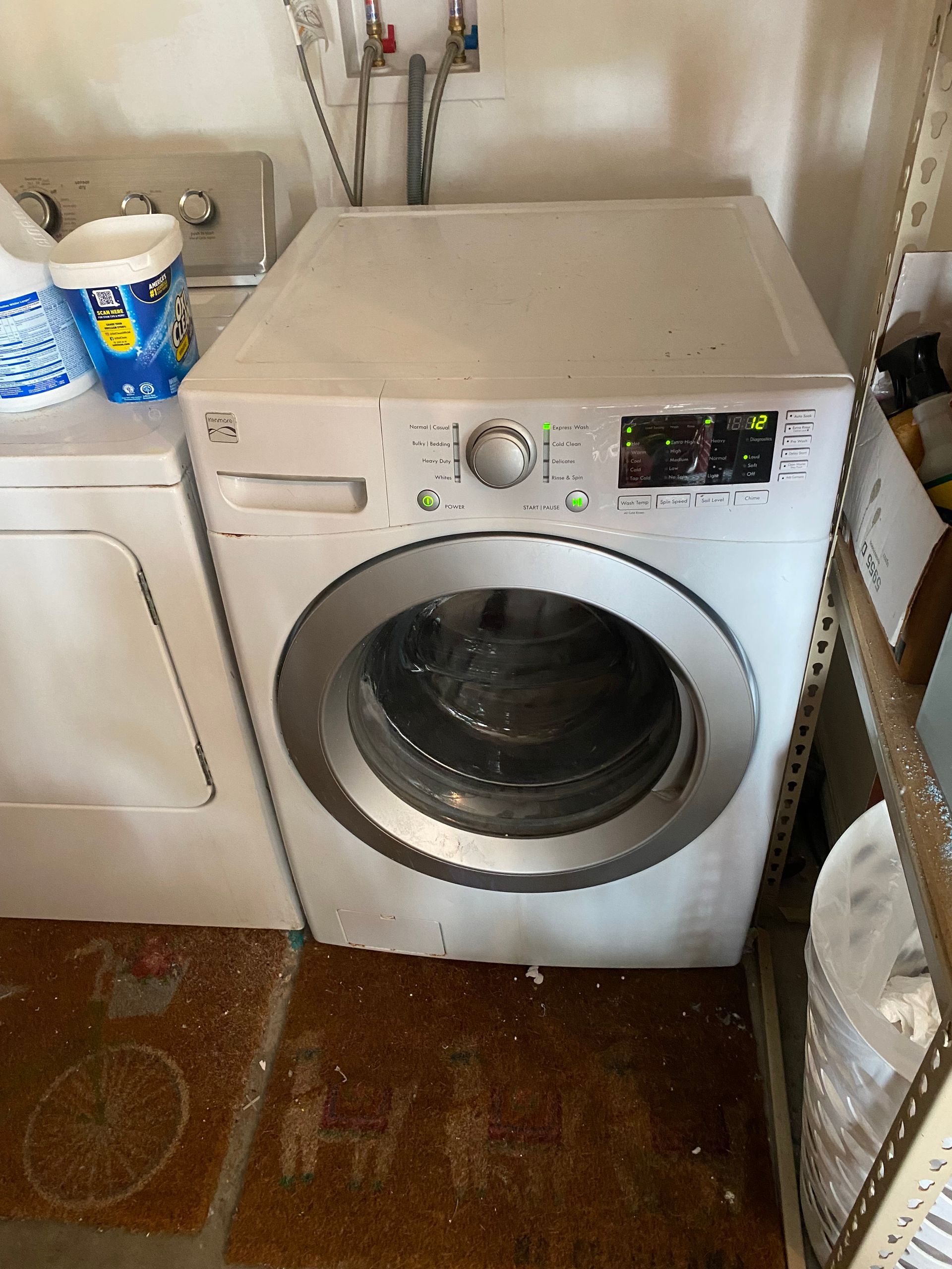 White LG washing machine in a laundry area, next to a dryer and shelving.