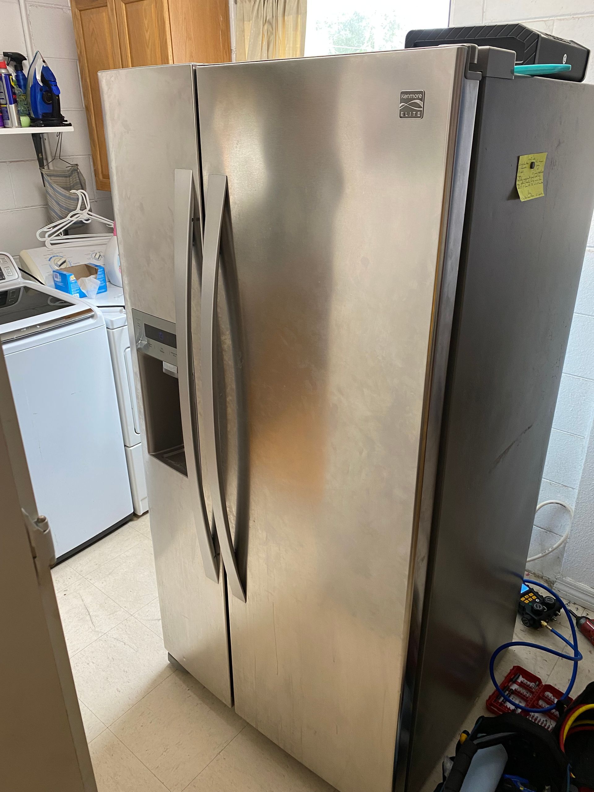 Stainless steel Kenmore side-by-side refrigerator in a kitchen next to a washing machine.