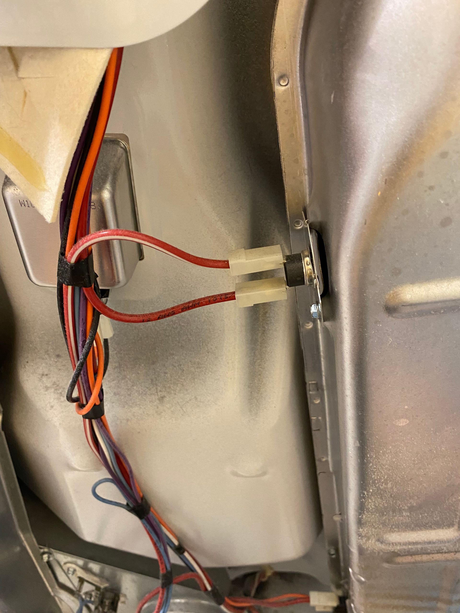 Close-up view of dryer interior, showing electrical wiring and terminals on the metal chassis. Red wires connected.