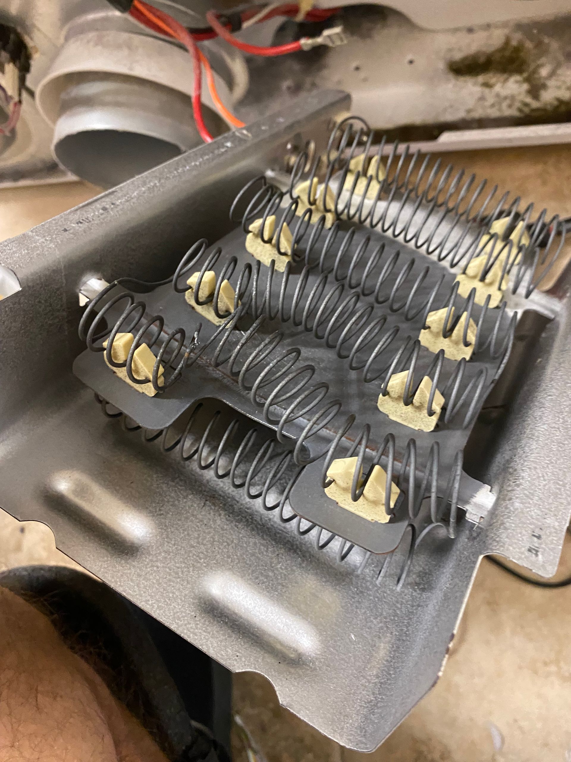 Close-up of a dryer's heating element, gray coils held in place by ceramic insulators within a metal housing.