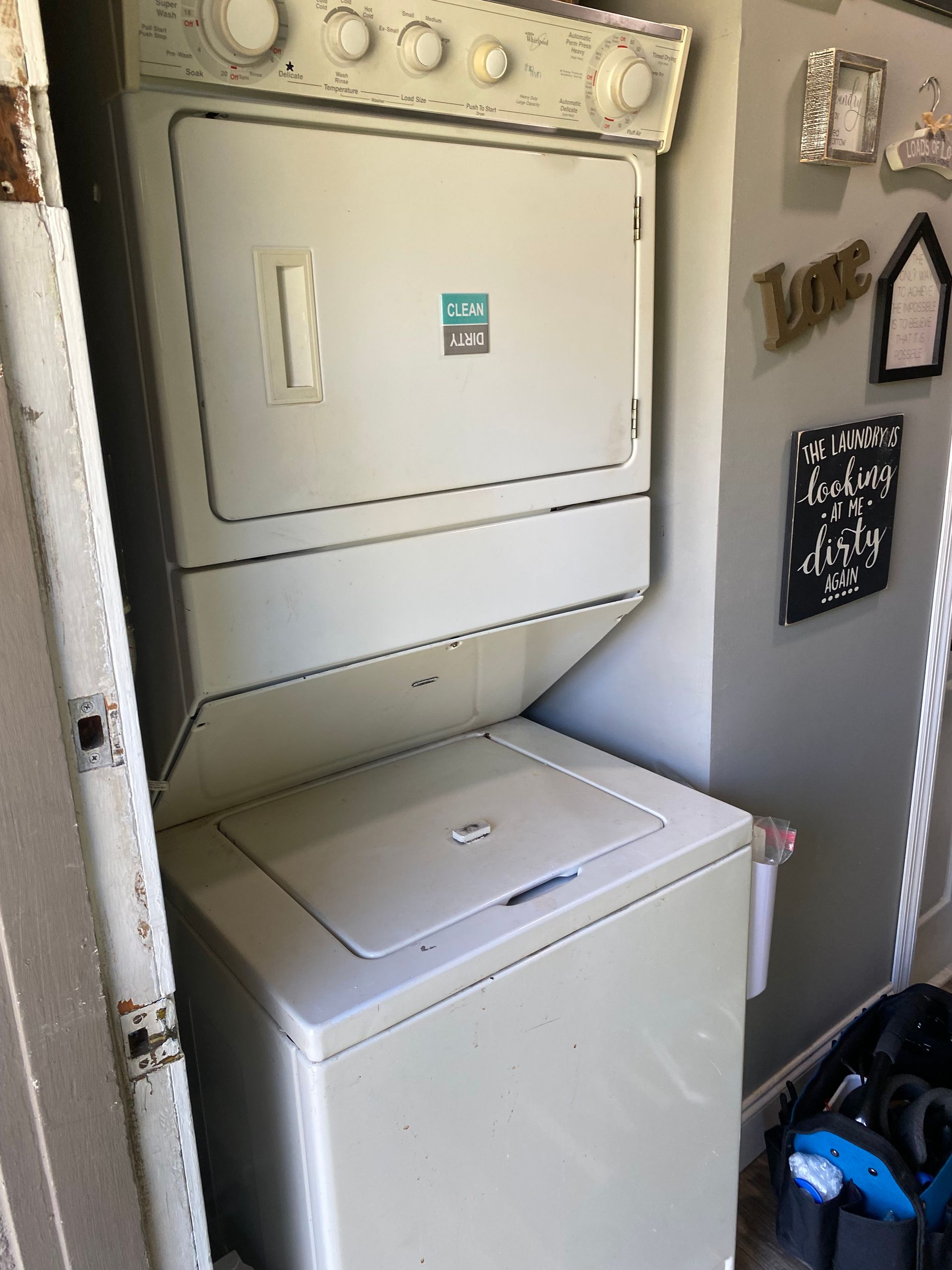 Stacked white washer and dryer in a laundry room, near a doorway and wall decor.